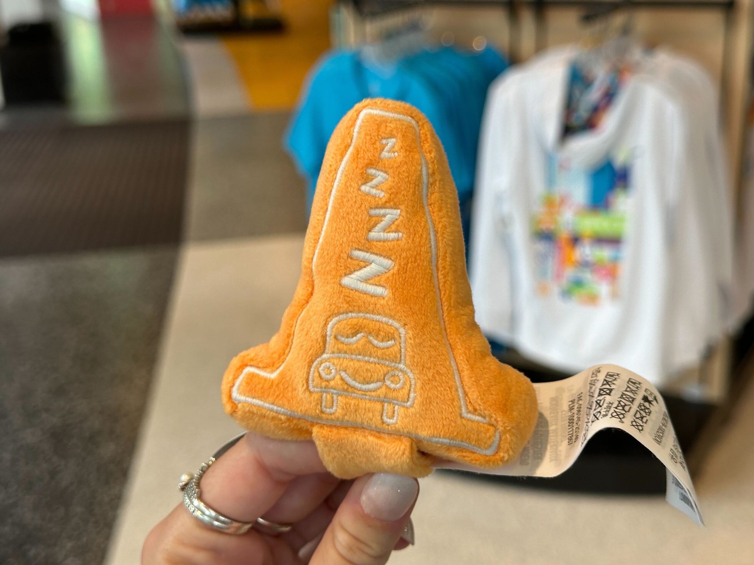 A hand holds a small orange plush shaped like a traffic cone from the Cars Plush Headband collection.