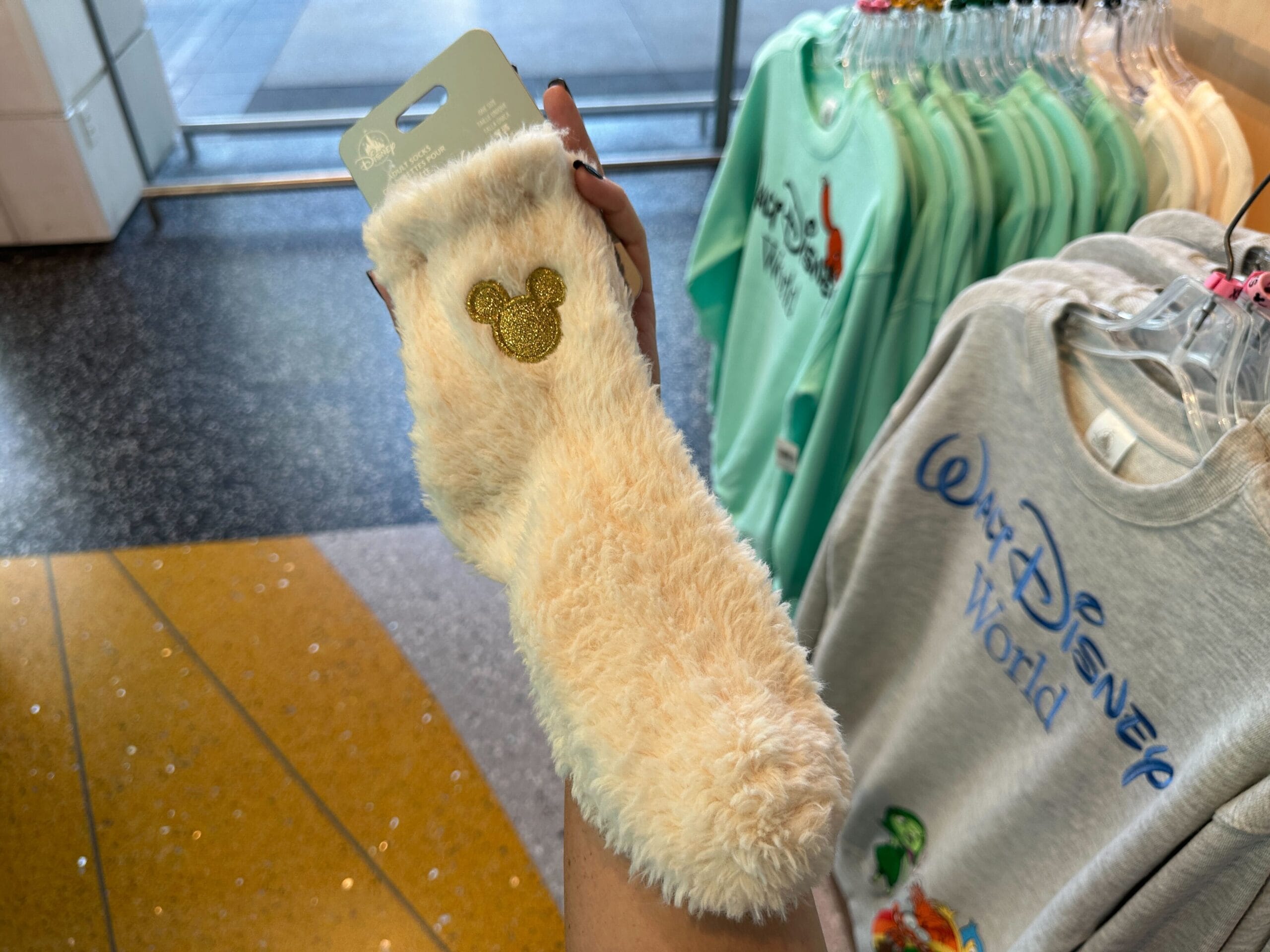 A hand holds novelty socks—a fuzzy cream pair with a gold Mickey logo—inside a Disney World gift shop.