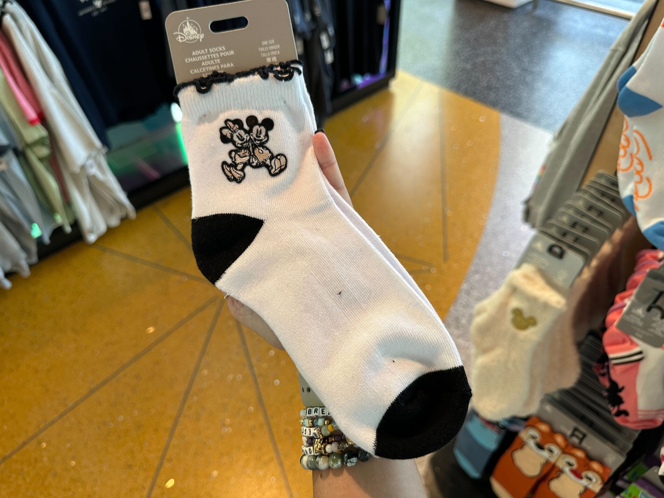 A hand holds a novelty sock with black accents and an embroidered image of Mickey and Minnie Mouse.
