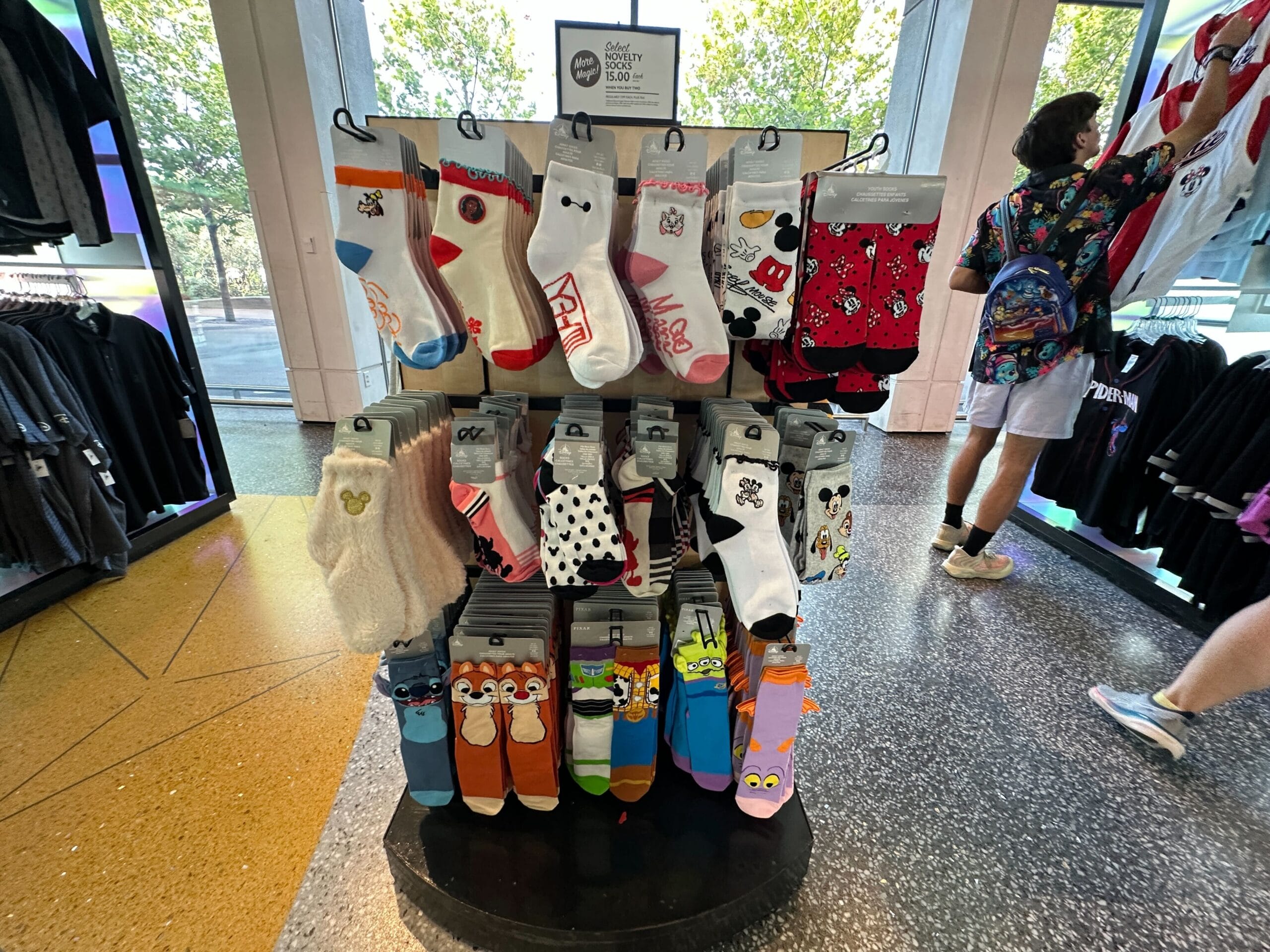 A display rack of colorful Disney World novelty socks, including Figment socks, with shoppers browsing in the background.