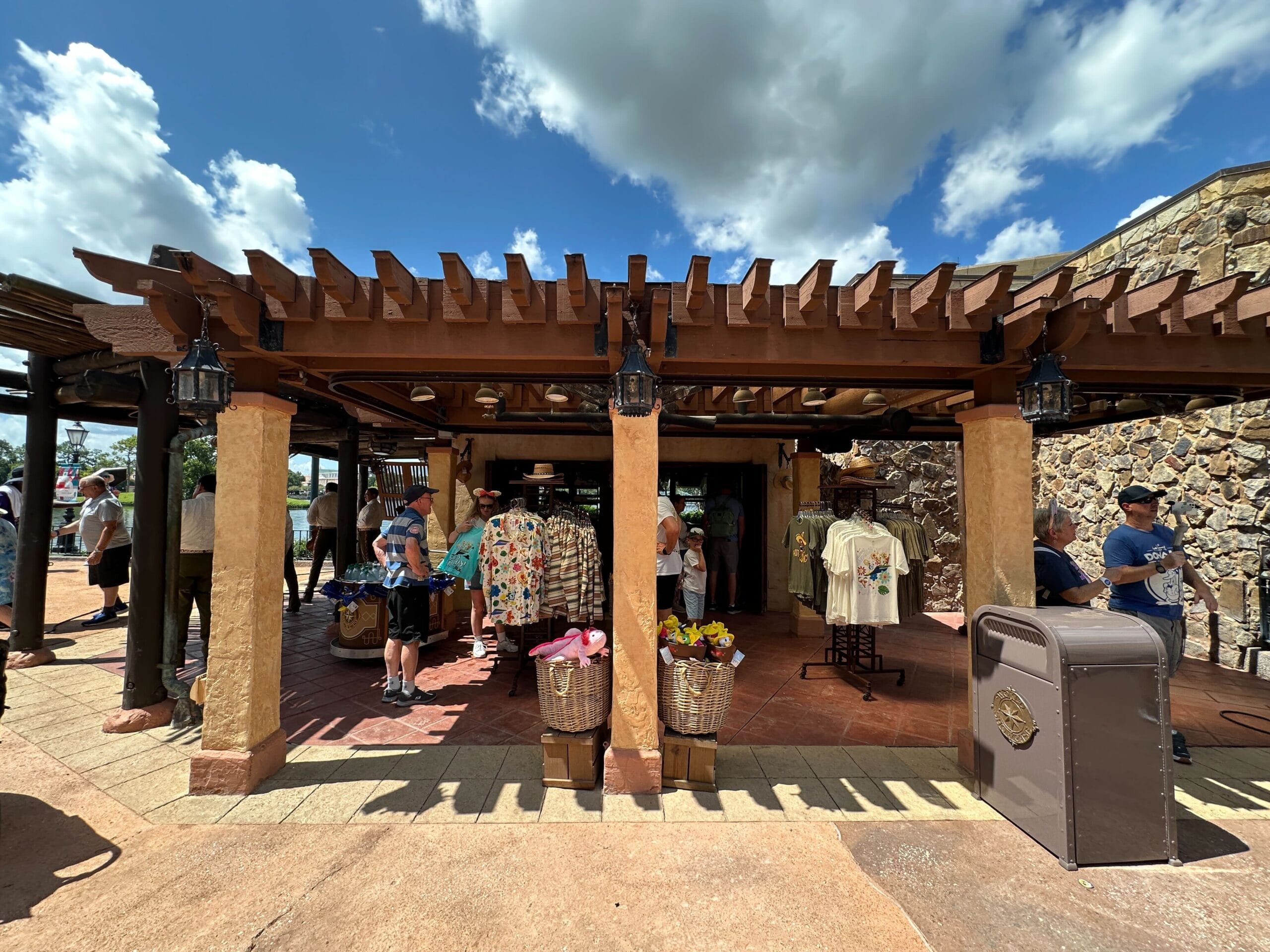 Outdoor gift shop at EPCOT’s Mexico Pavilion with shirts, plush toys, and visitors browsing El Ranchito del Norte.