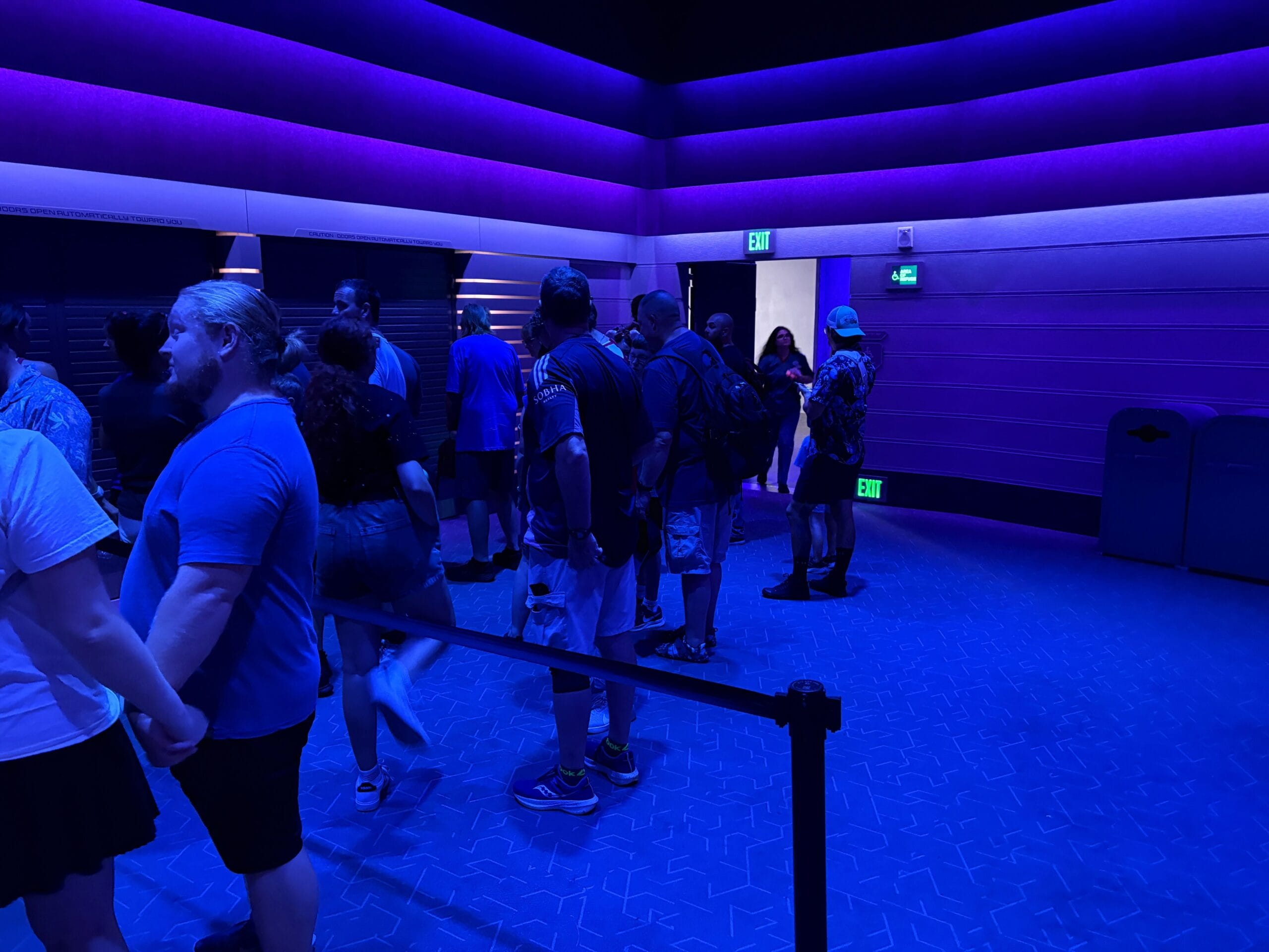 People queue inside a room with blue and purple lighting and geometric walls, part of the Guardians of the Galaxy: Cosmic Rewind.