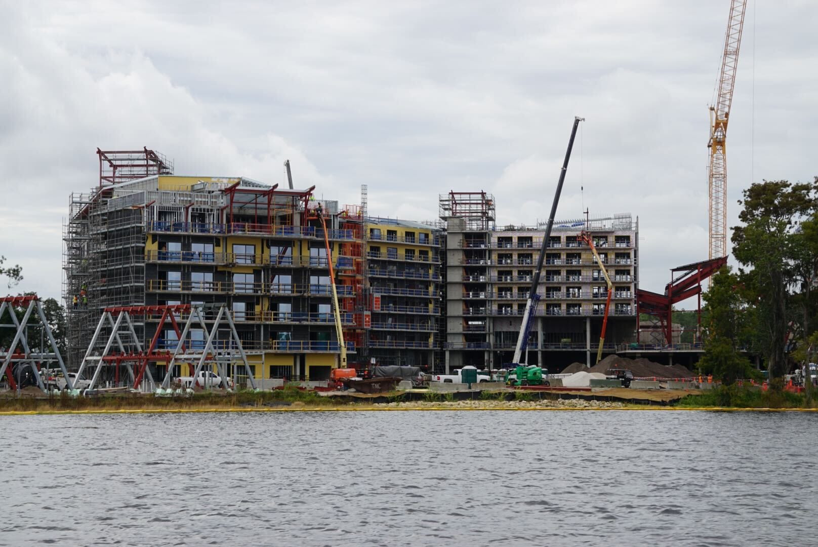 Lakeshore Update: A large building under construction by the lakeshore, cranes and scaffolding beneath a cloudy sky.