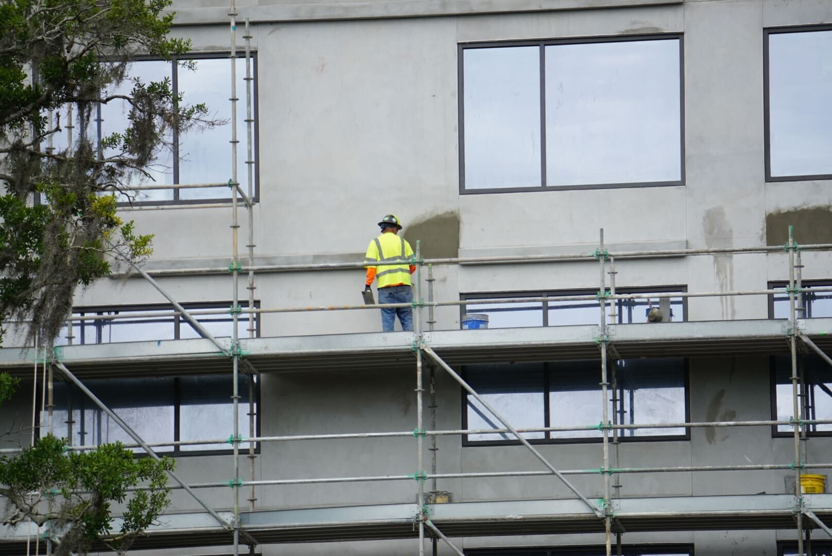 A construction worker in a yellow vest stands on scaffolding during the Lakeshore Update, working on the building’s exterior wall.