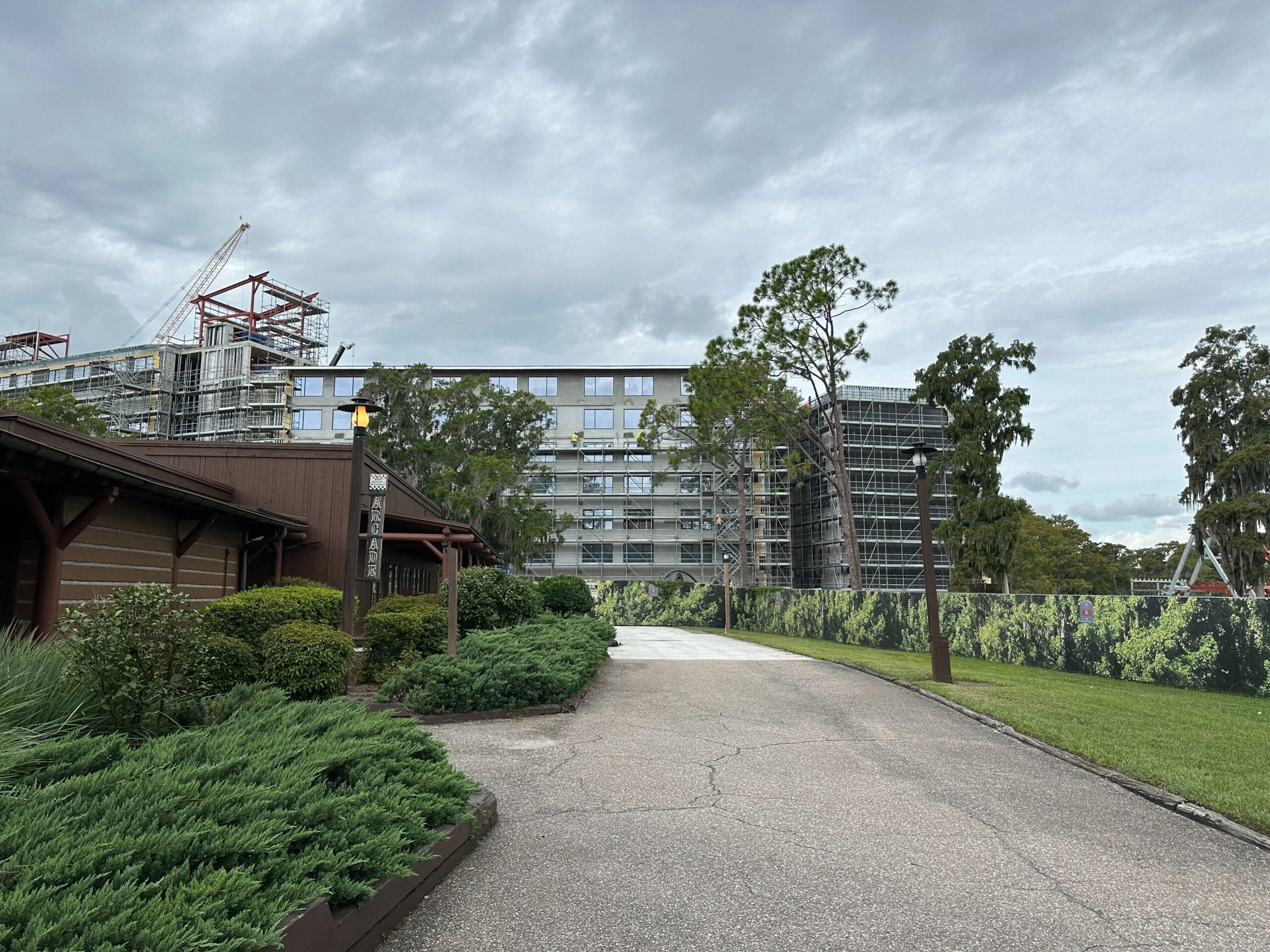 A paved path by Lakeshore leads past a brown building to a large hotel under construction with scaffolding and cranes.