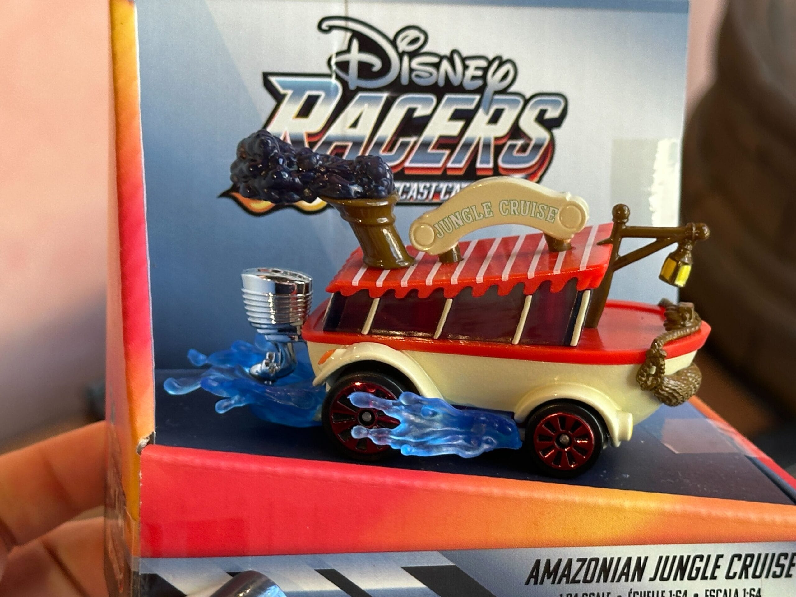 A Disney Racers Toy car modeled after the Jungle Cruise boat, with blue flames and Disney World packaging in the background.