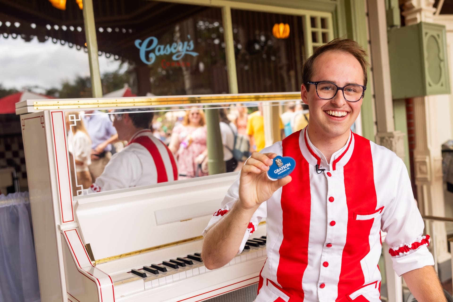 Grayson Smith, Casey's Corner Pianist, smiles in red and white with a blue "I'm celebrating" button by the piano.