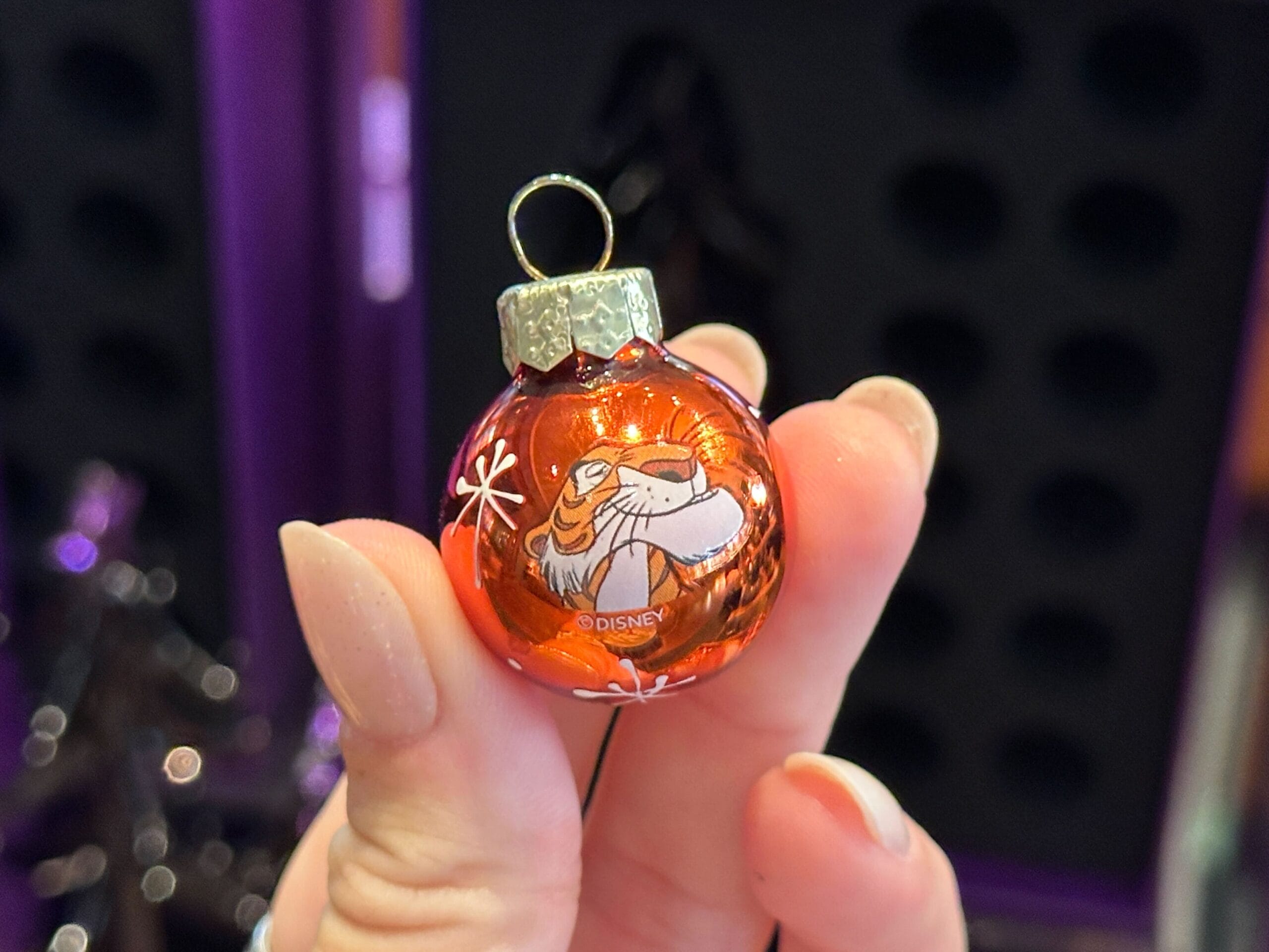 A hand holds a small orange Disney Villain Ornament featuring Tigger's face from Winnie the Pooh.