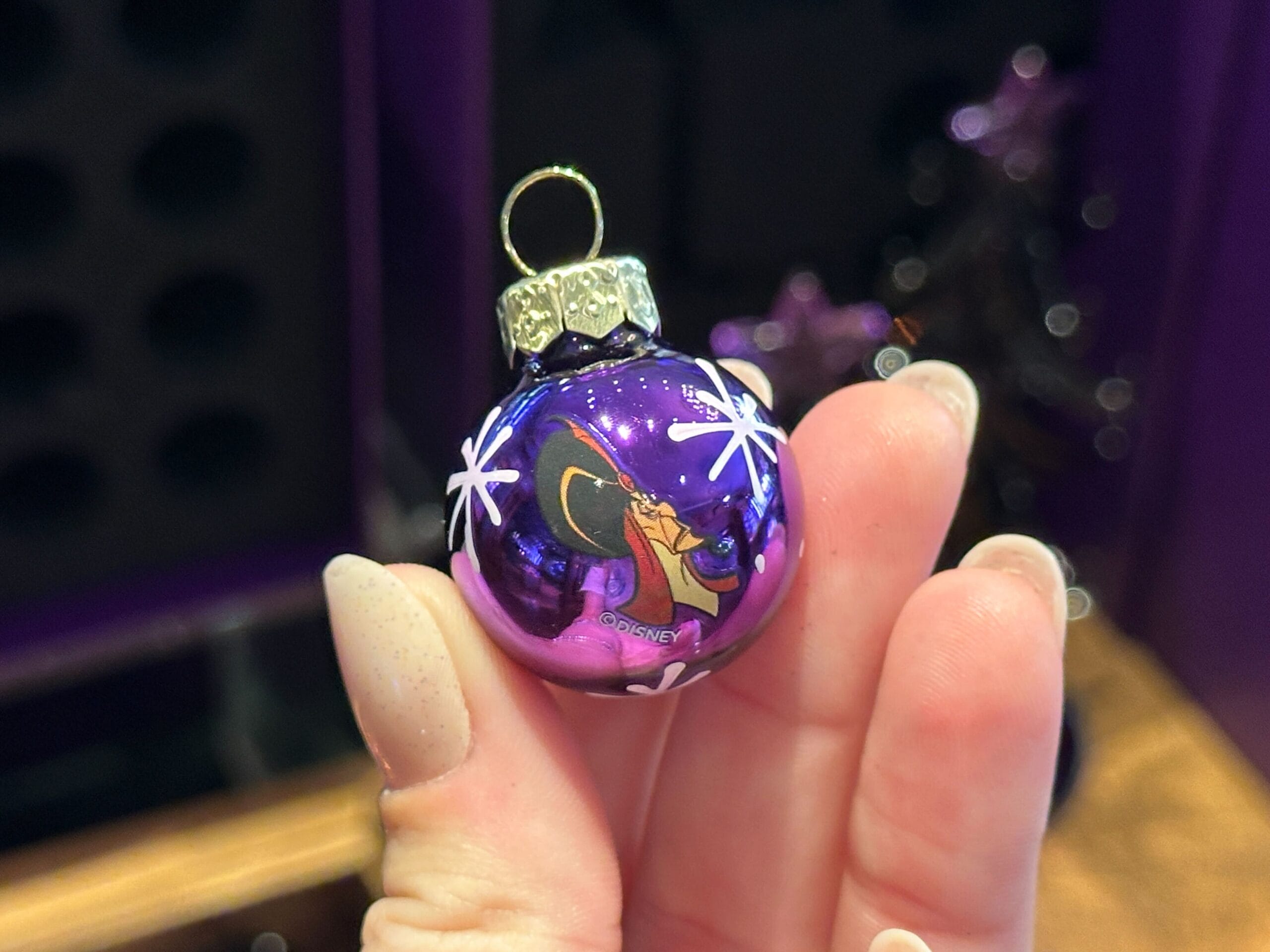 A hand holds a small purple Villain Ornament featuring a cartoon character and white star patterns.