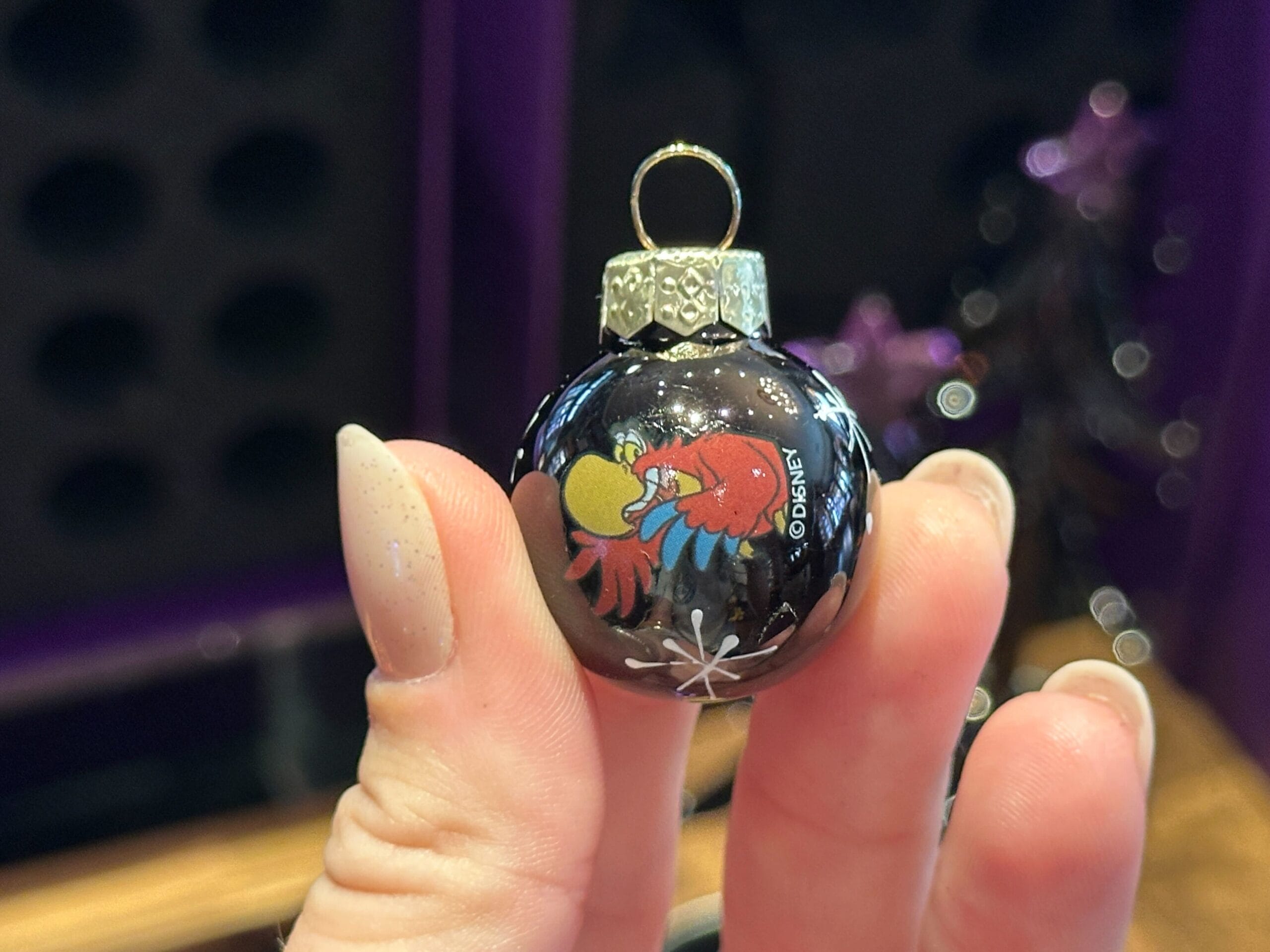 A hand holds a small black Disney World ornament featuring Kermit the Frog and Miss Piggy kissing.