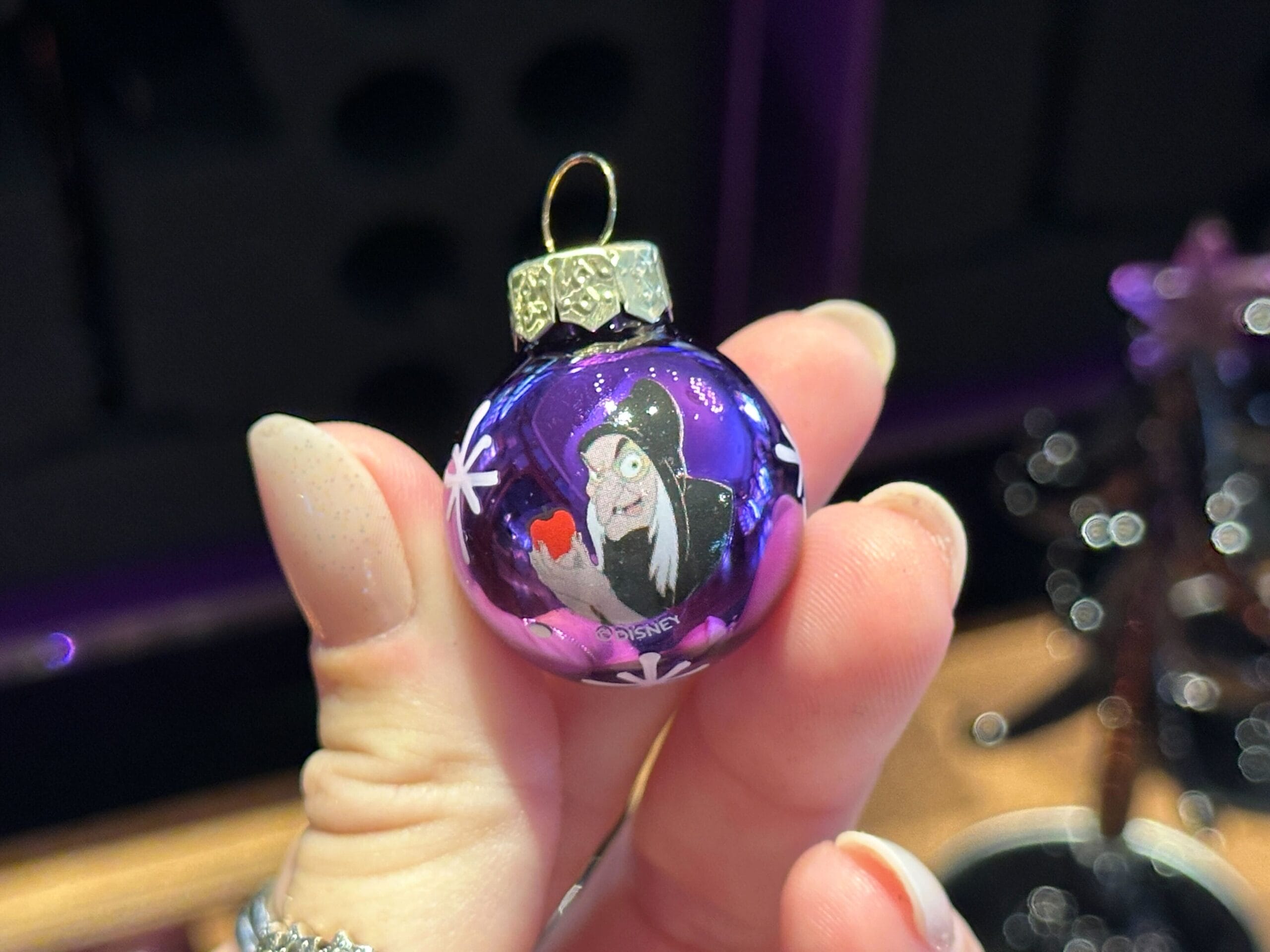 A hand holds a purple villain ornament featuring Disney's Evil Queen in disguise with an apple.