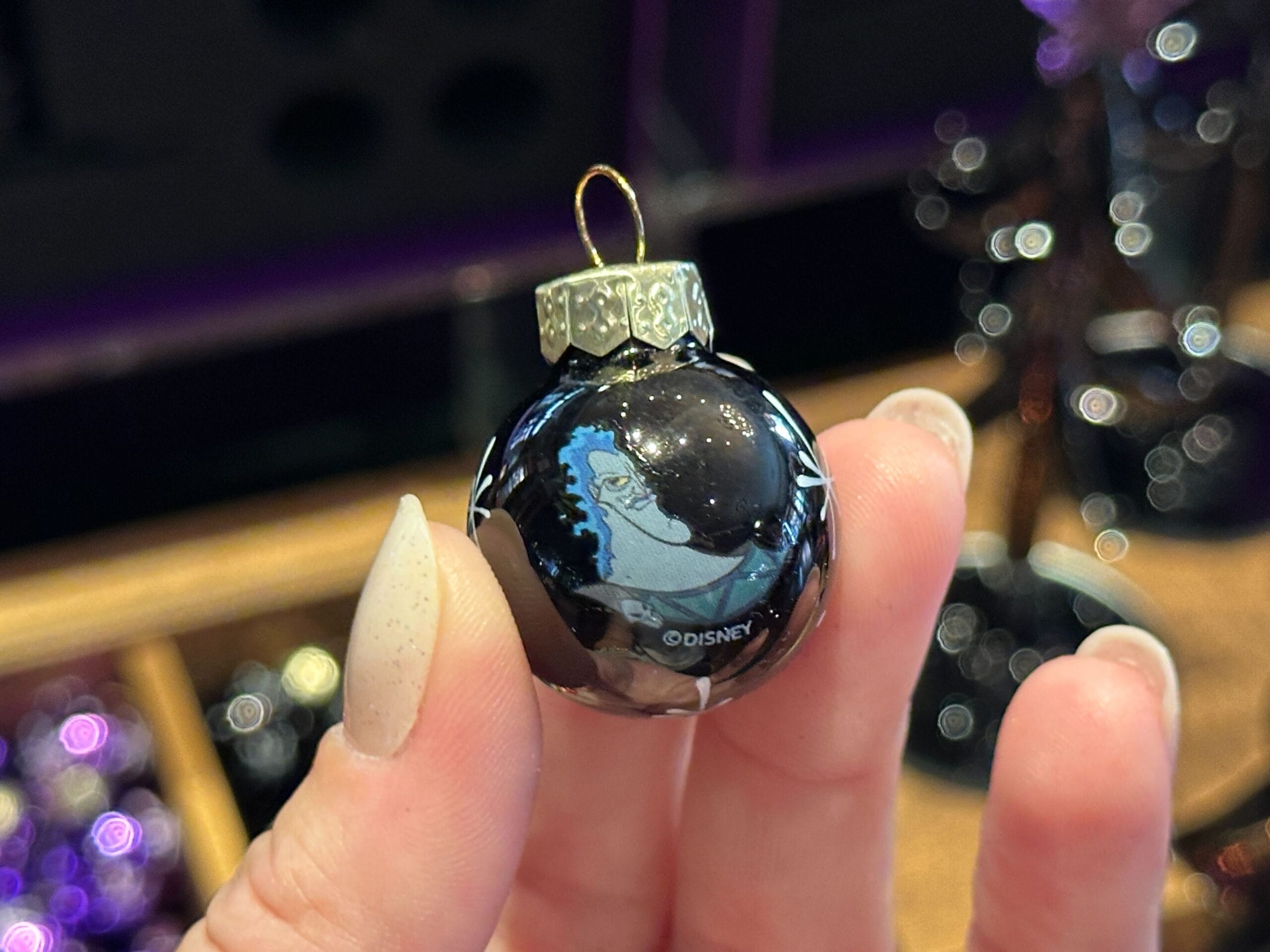 A hand holds a Villain Ornaments black Hades ornament with a gold cap, perfect for Disney World fans.