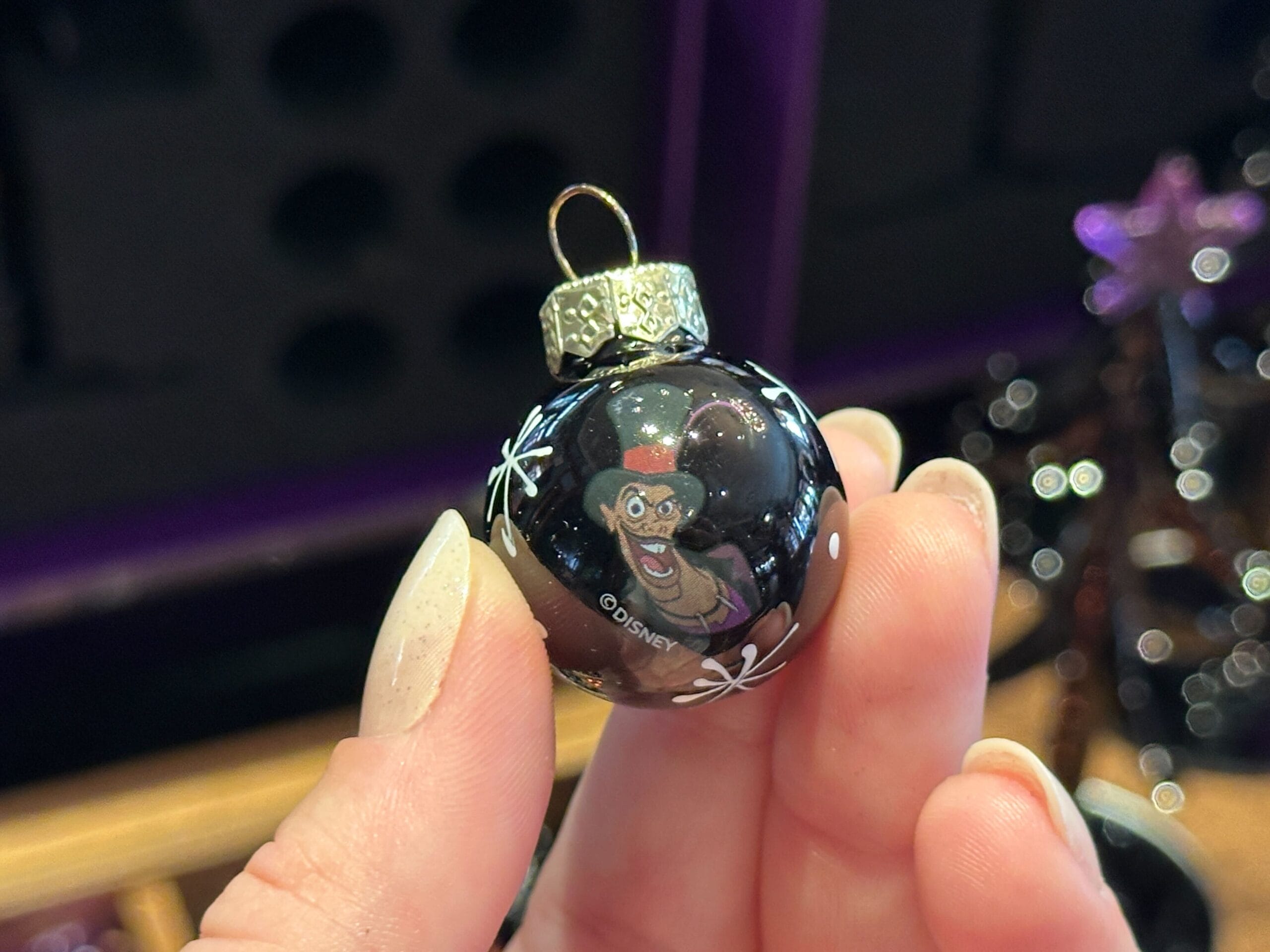 A hand holds a black Villain Ornament featuring a grinning cartoon villain wearing a top hat.