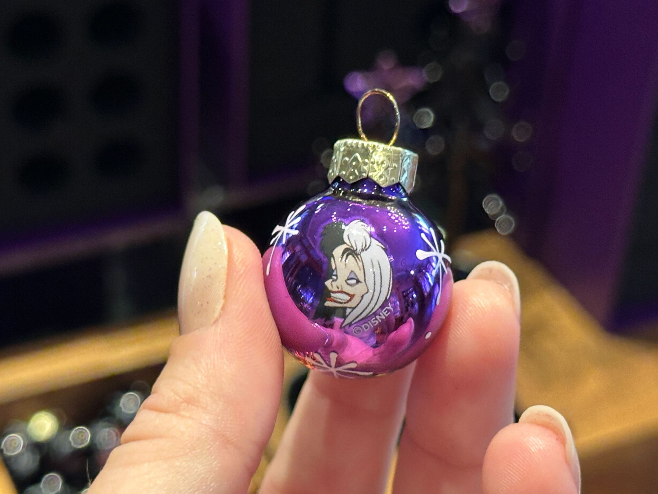 A hand holds a purple villain ornament featuring a cartoon woman with white hair and a mischievous smile.
