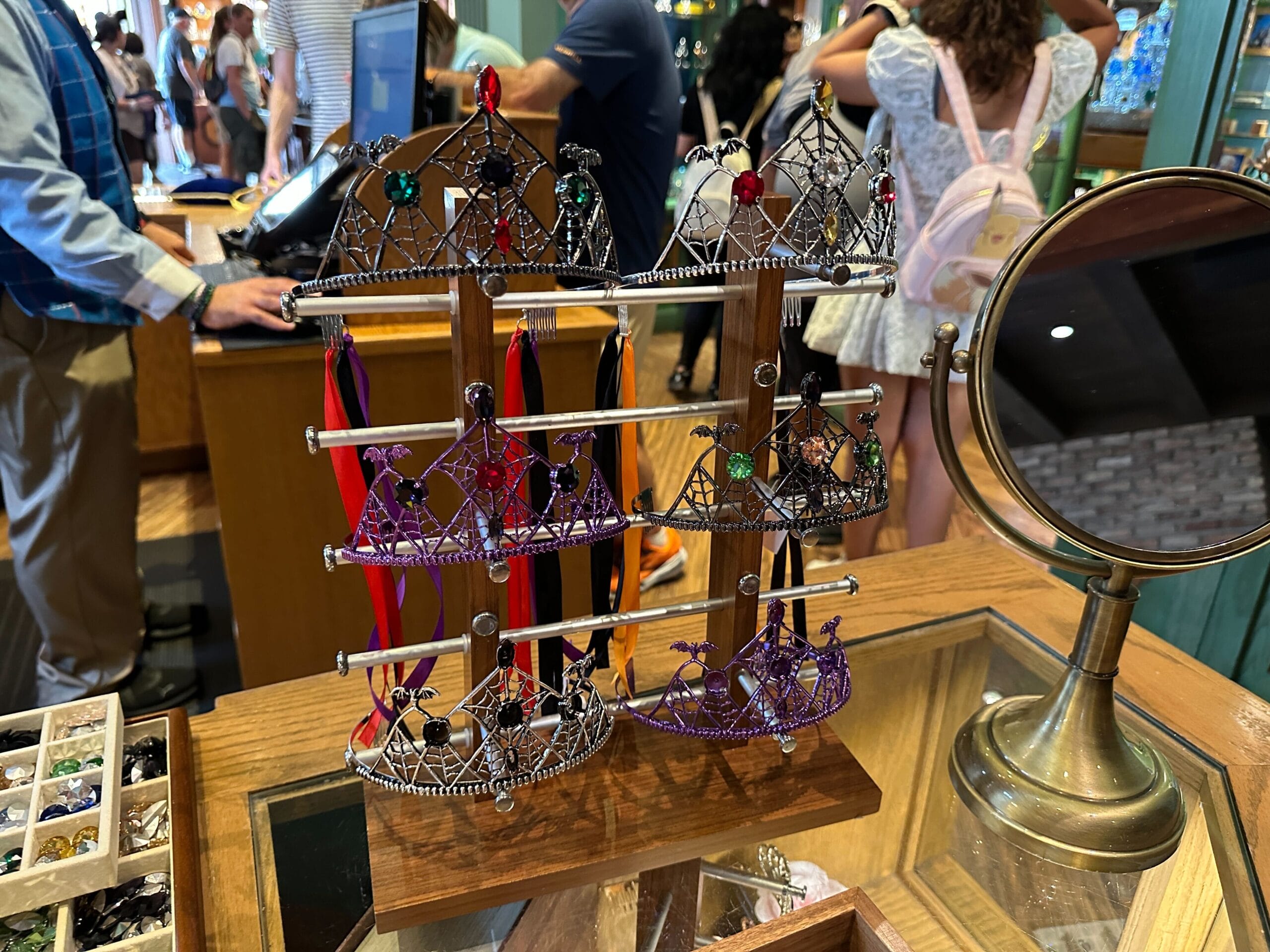 Customizable wire crowns with colored jewels are displayed on a stand, perfect as Halloween tiaras for Disney World fans.