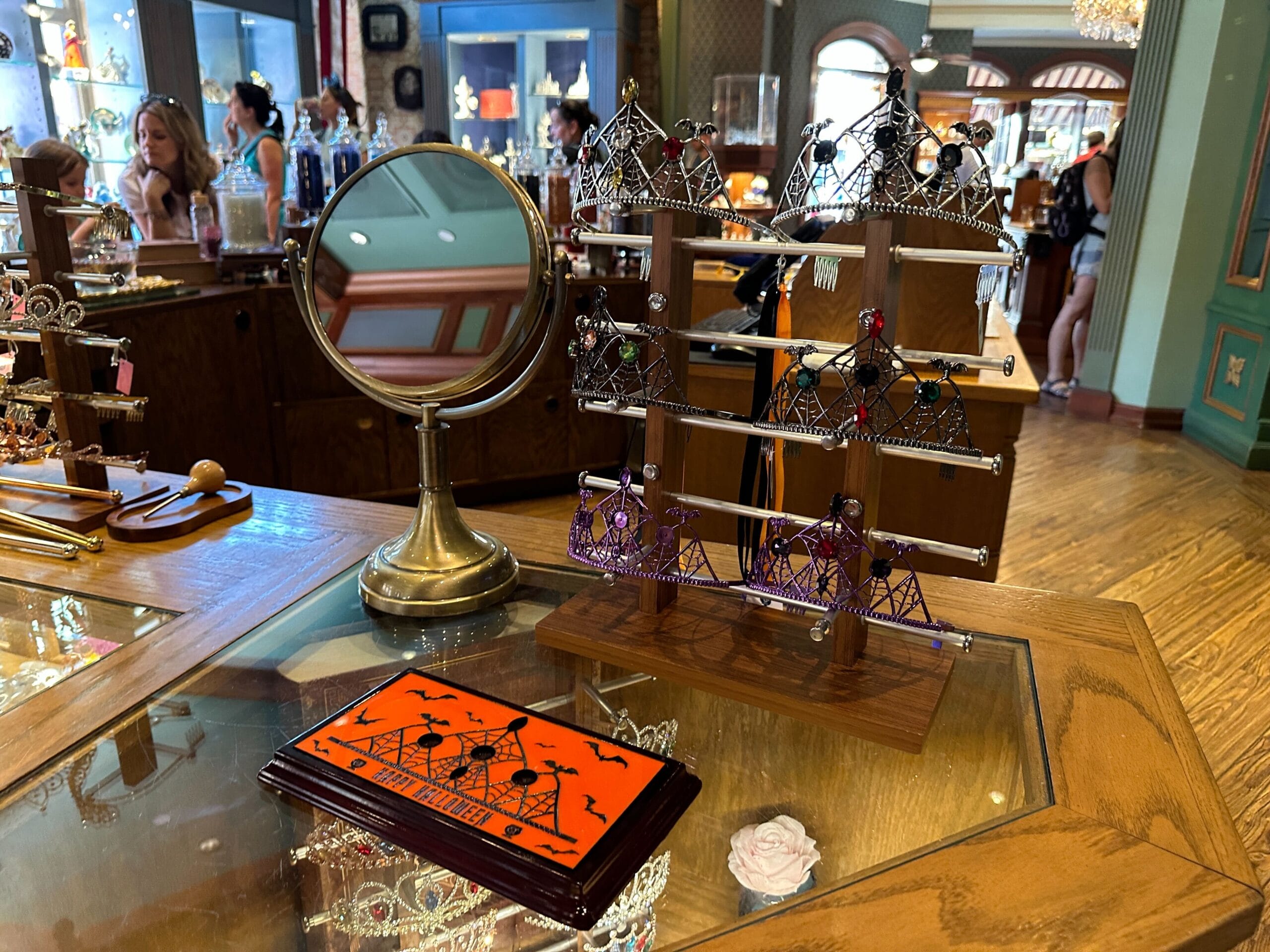 Jewelry display with customizable Halloween tiaras, mirror, and Disney World-themed card on a boutique shop counter.