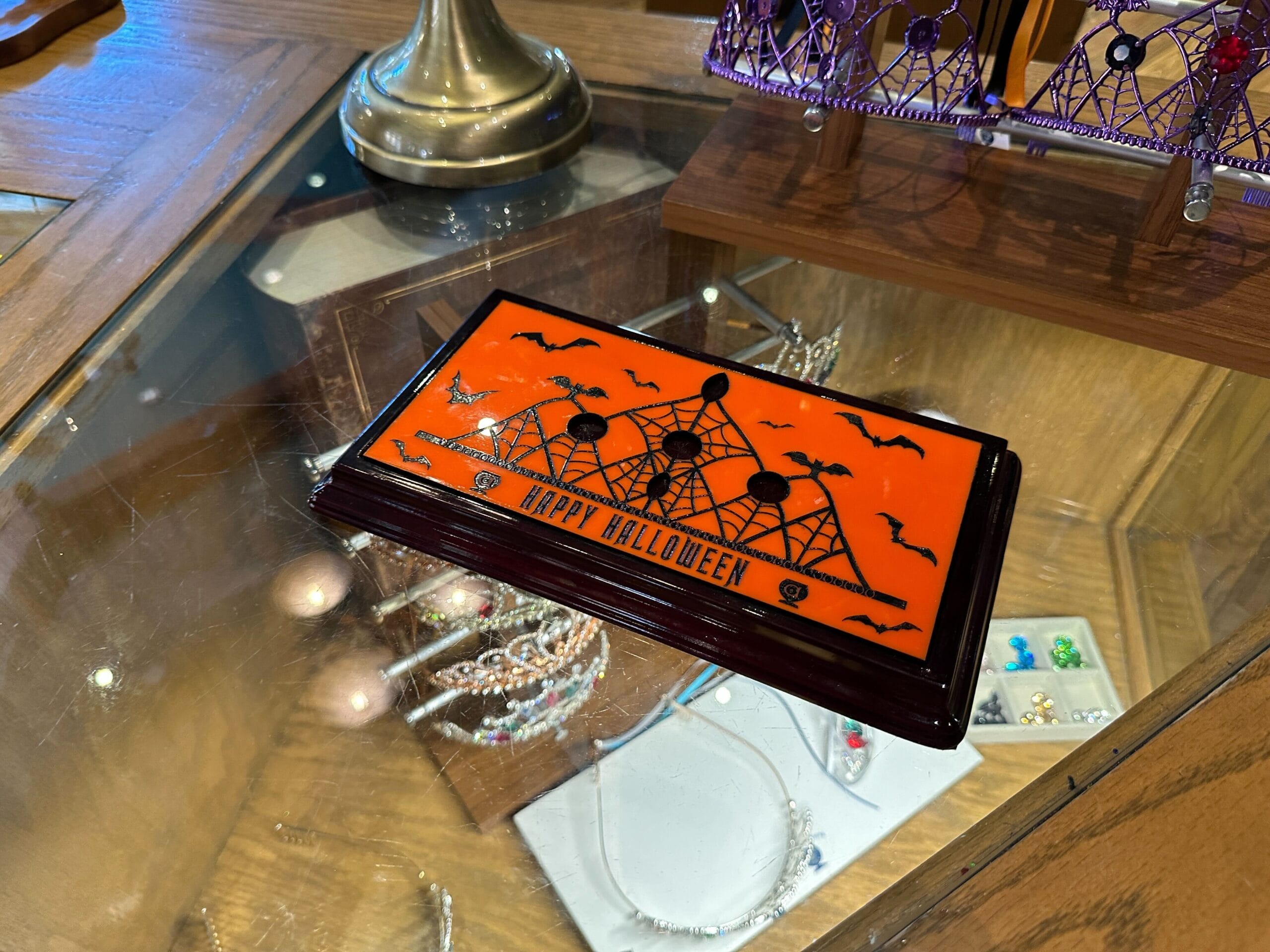 An orange sign with bats and a haunted house sits atop a glass display of customizable Halloween tiaras.