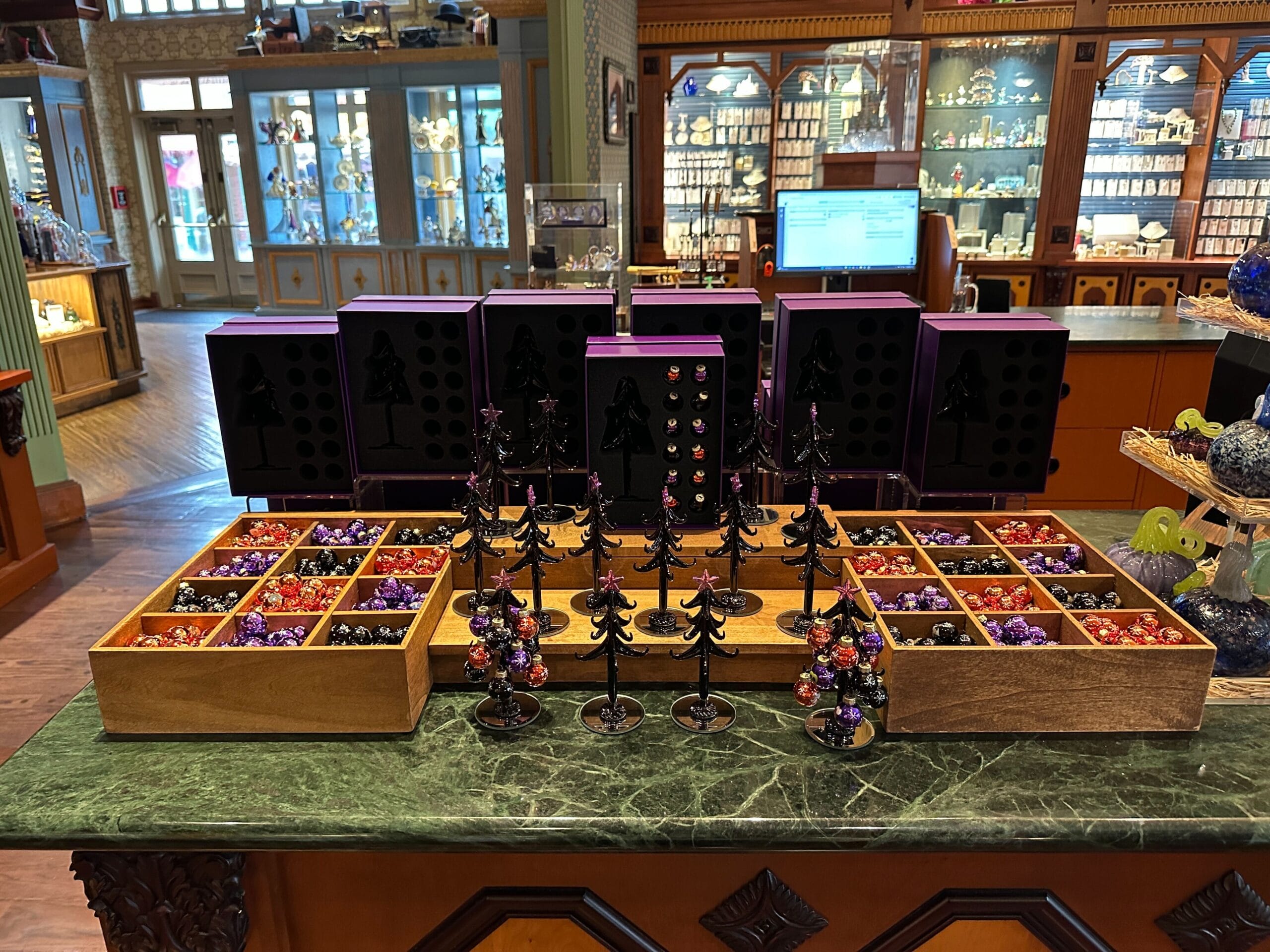Display of colorful Christmas ornaments, villain ornaments, and jewelry on a marble counter in a decorative store setting.