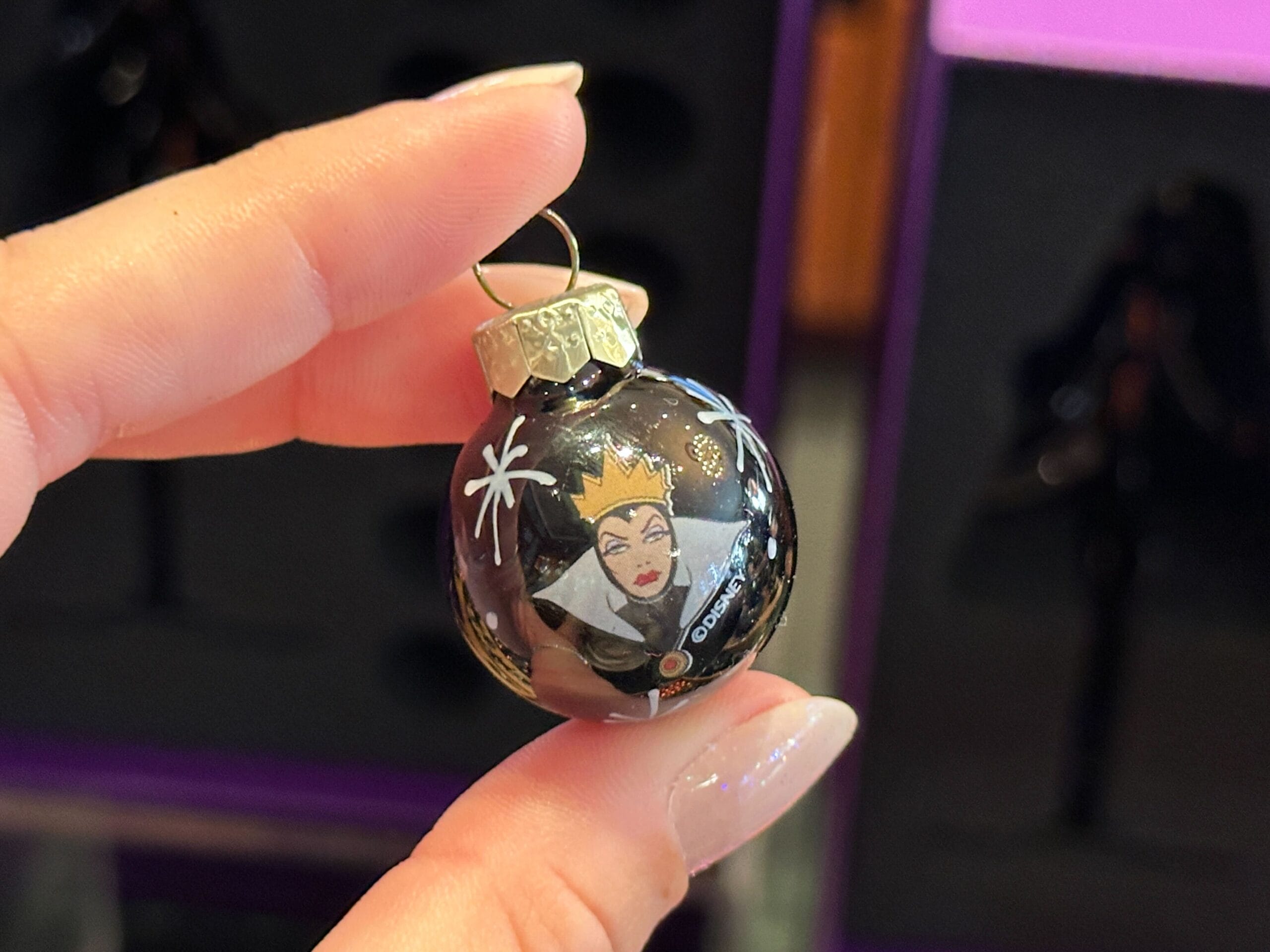 A hand holds a Disney World Villain Ornament of the Evil Queen from Snow White, adorned with white stars.