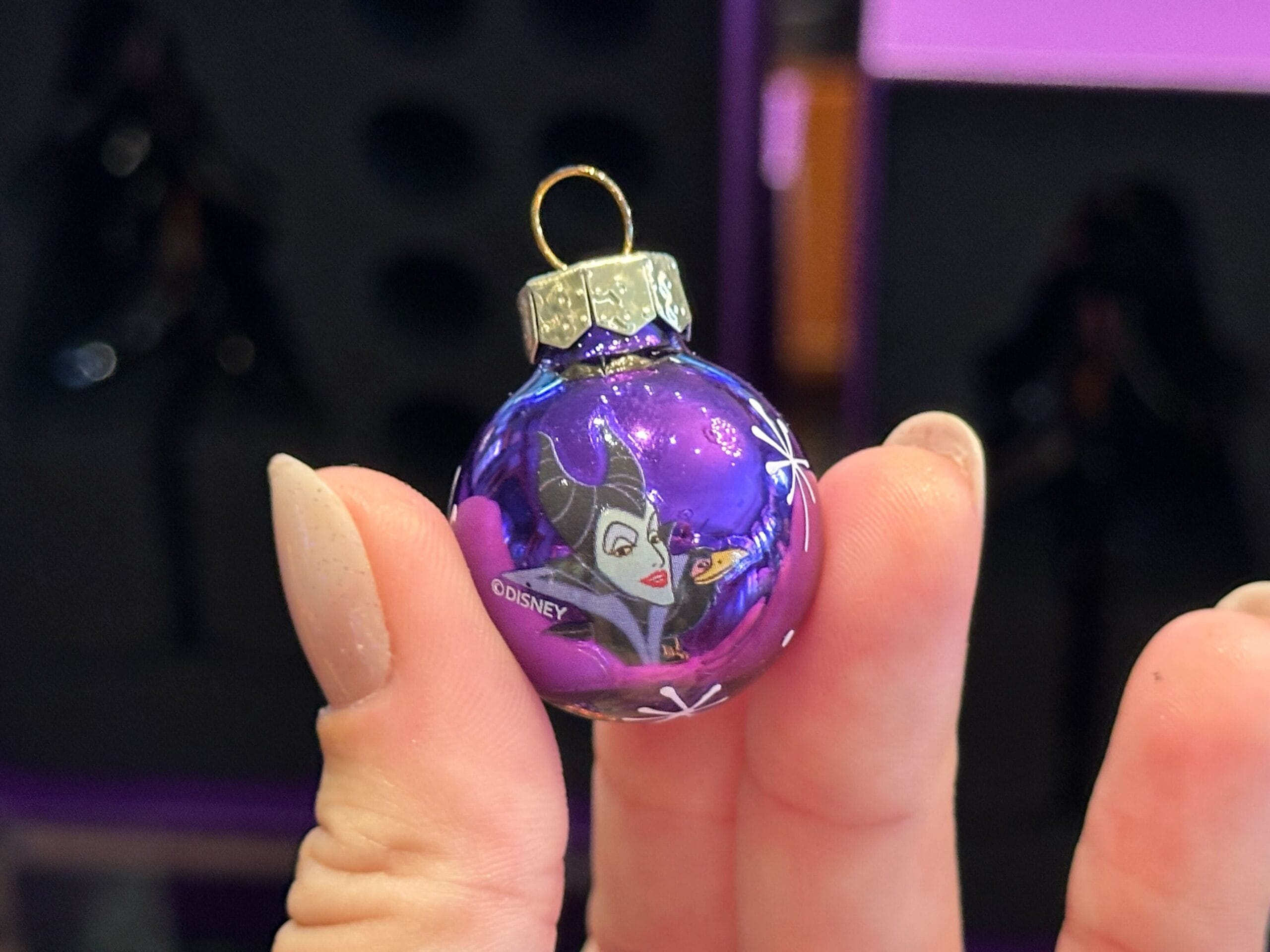 A hand holds a small purple Villain Ornament featuring Disney's Maleficent, perfect for Halloween Glass Trees.