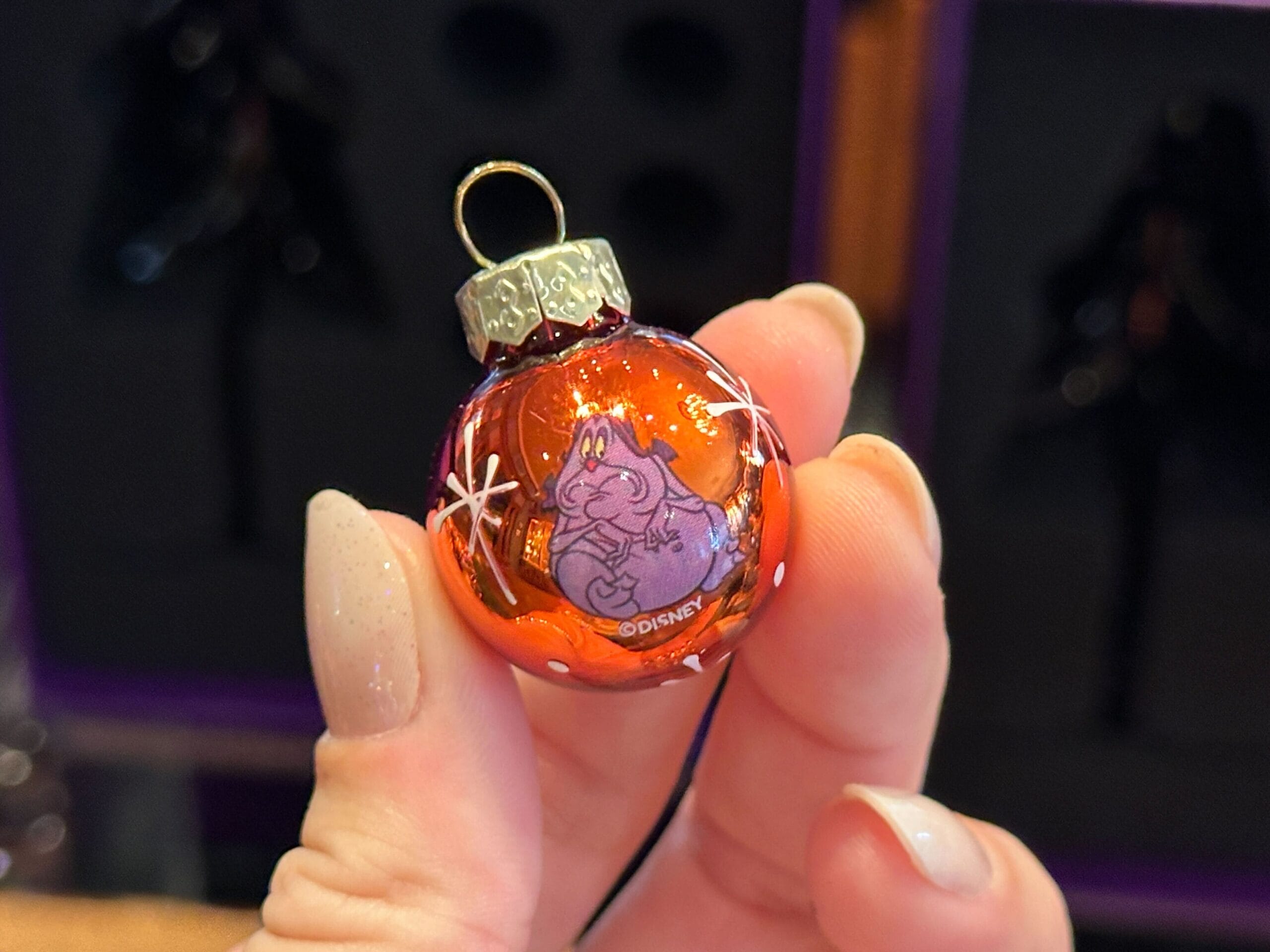 A hand holds a small red Disney Villain ornament with a smiling cartoon ghost and white star accents.