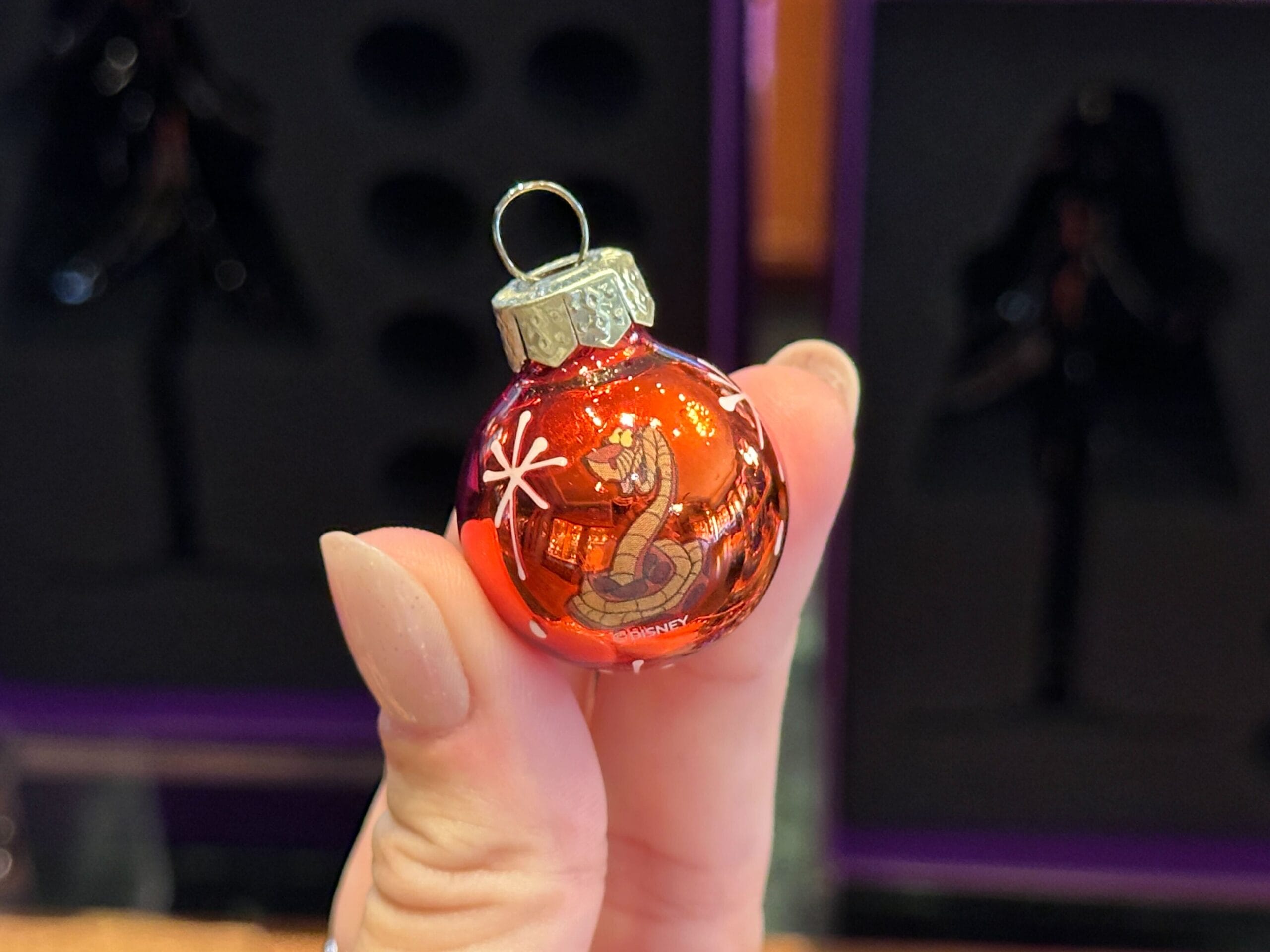 A hand holds a shiny red Christmas ornament from Disney World, decorated with a house and snowflakes.