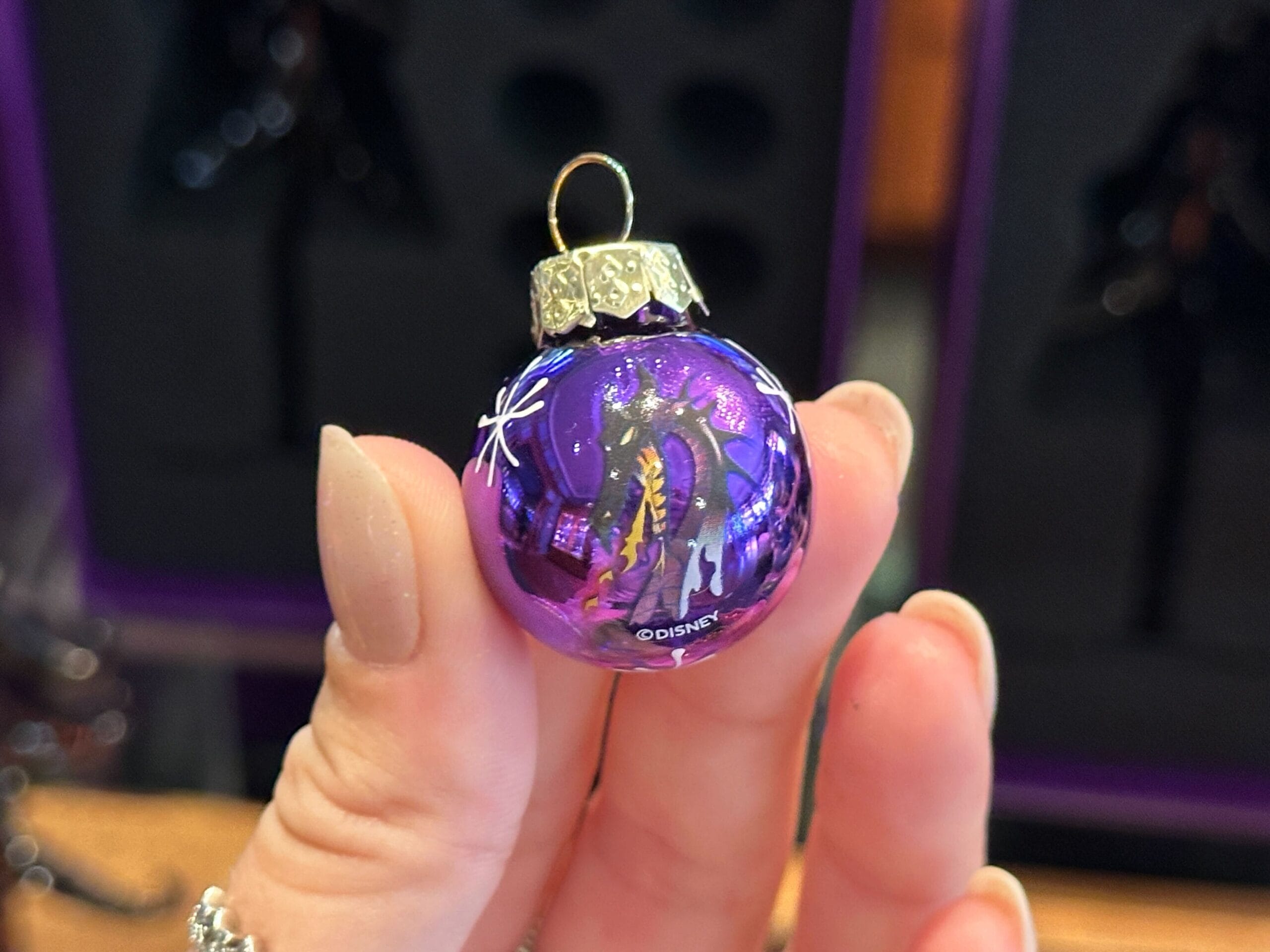 A hand holds a shiny purple Villain Ornament with a dragon design and gold cap, perfect for Halloween Glass Trees.