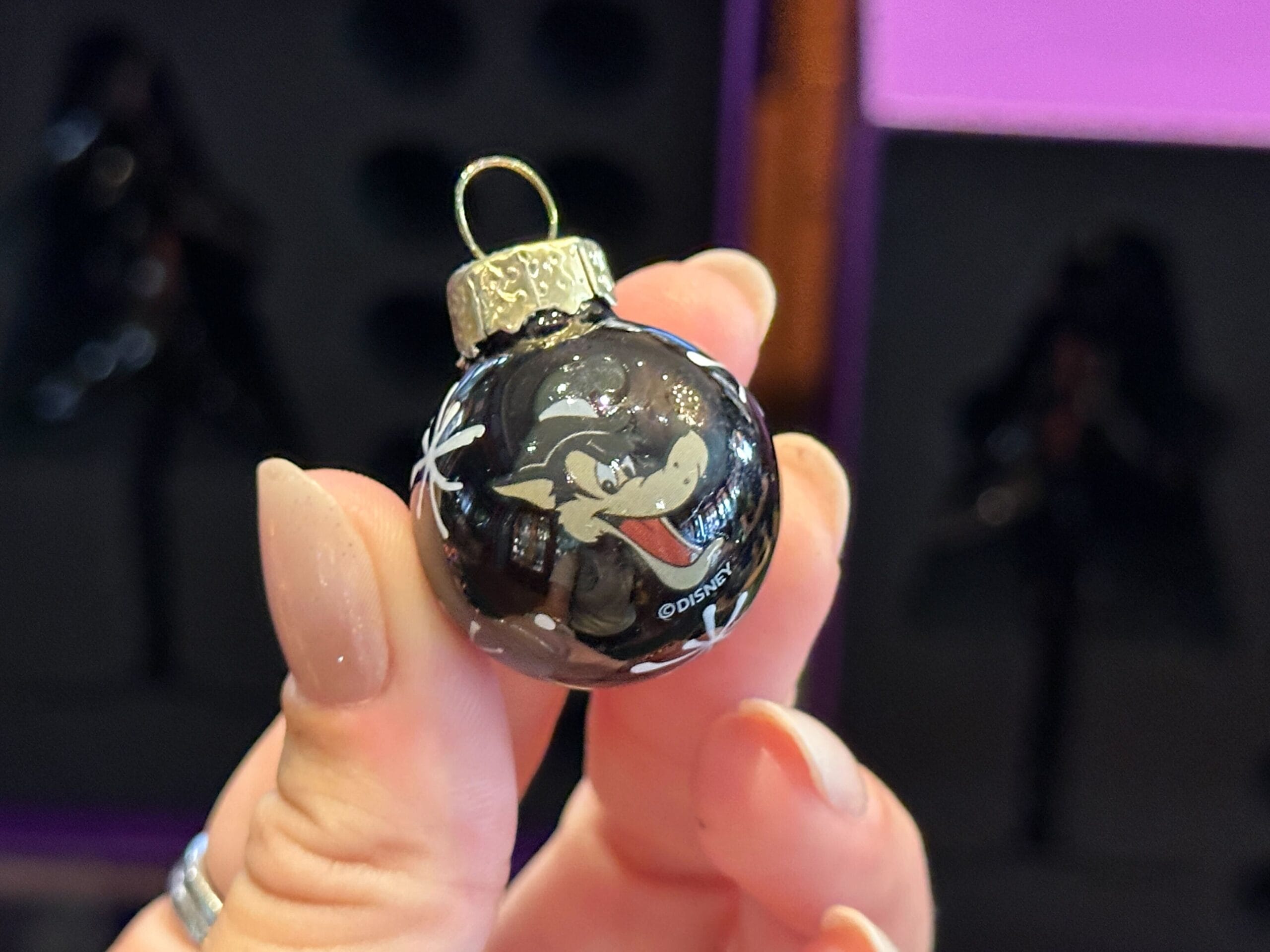 A hand holds a small black Villain Ornament featuring Disney's Big Bad Wolf cartoon character.