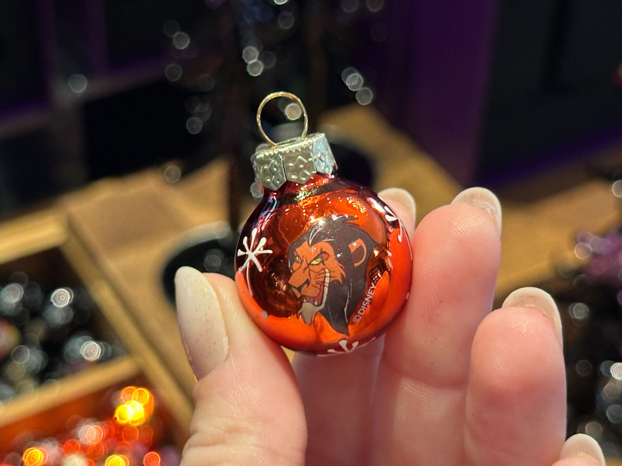 Hand holding a red Disney World Villain Ornament of Scar from The Lion King, with white snowflake designs.