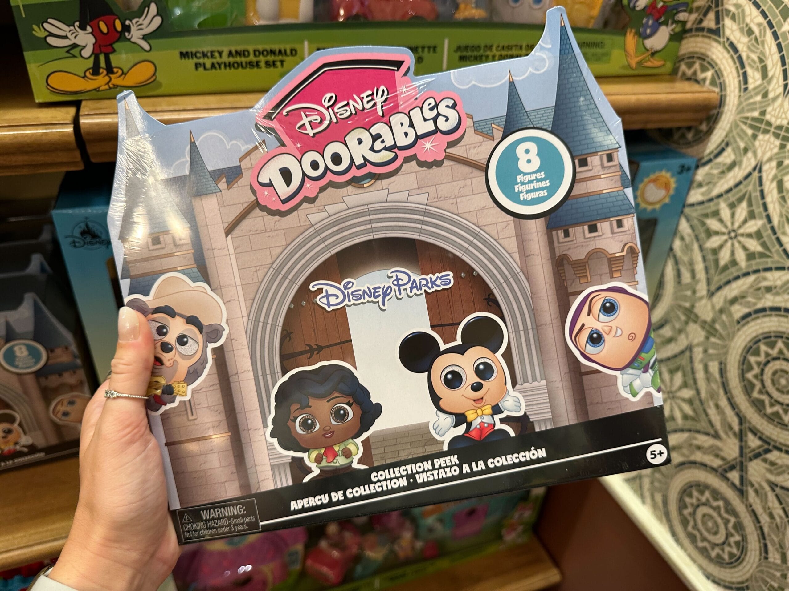 Hand holding a Disney Doorables toy box featuring Disney Parks Characters like Mickey Mouse on the front.