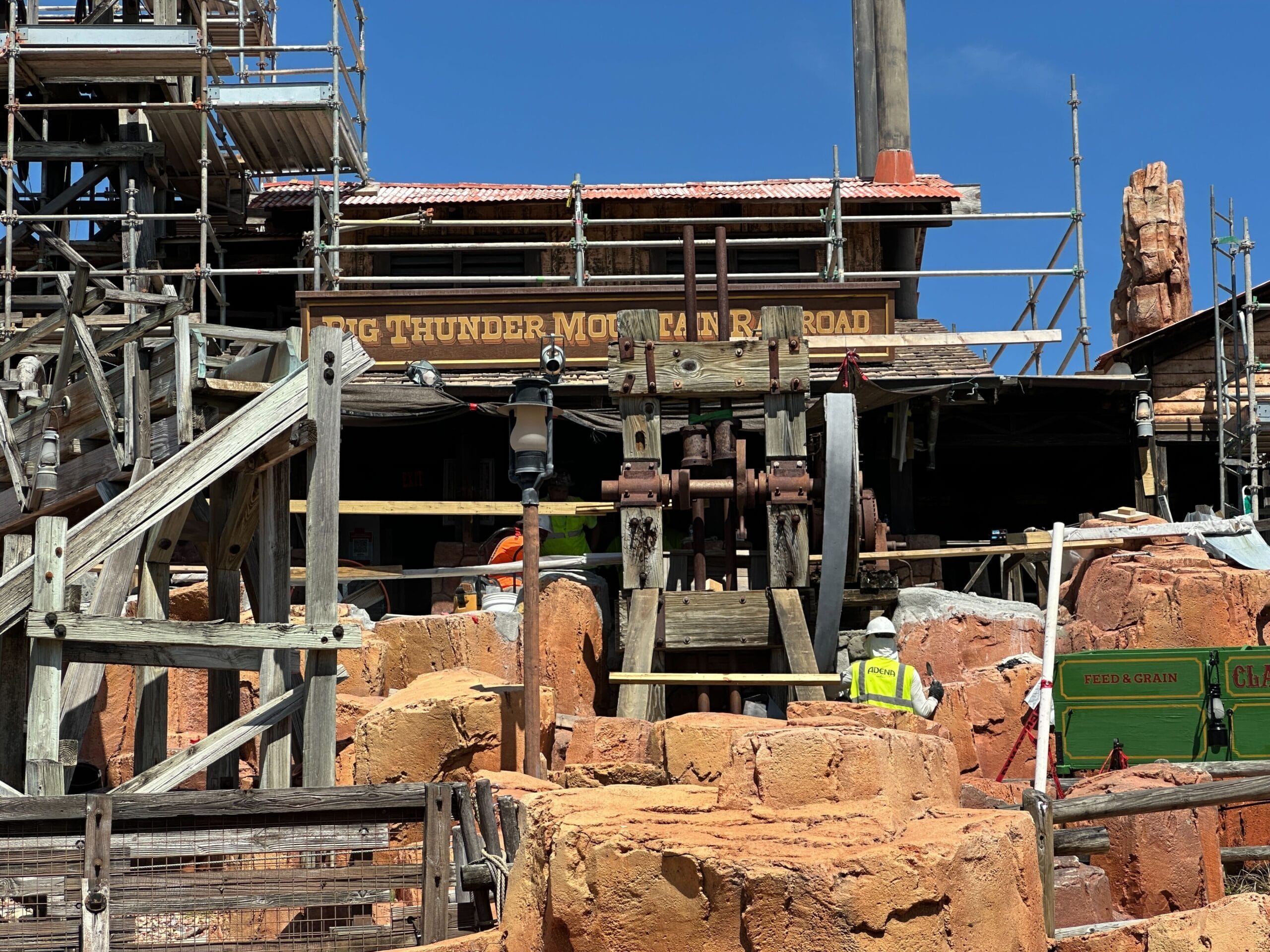 Construction workers in safety vests repair Big Thunder Mountain, showing rockwork progress amid scaffolding and rocks.