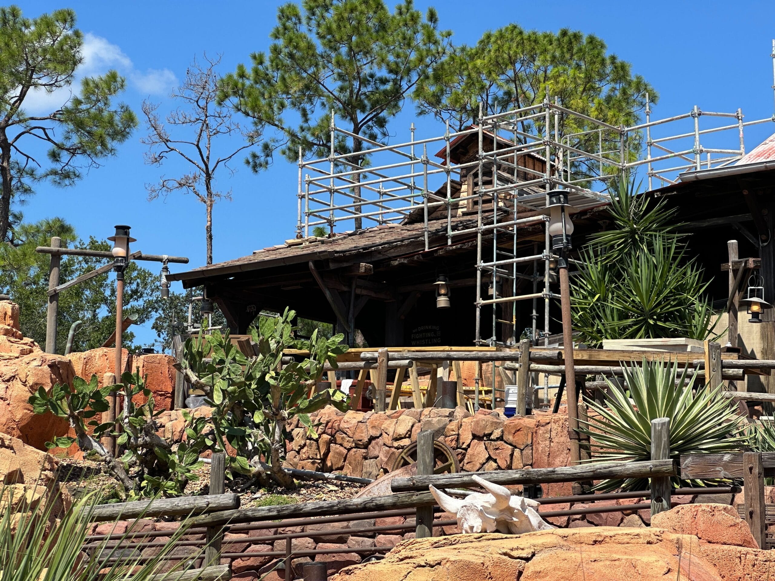 Big Thunder Mountain rockwork progress: wooden building construction with scaffolding amid desert plants under a blue sky.
