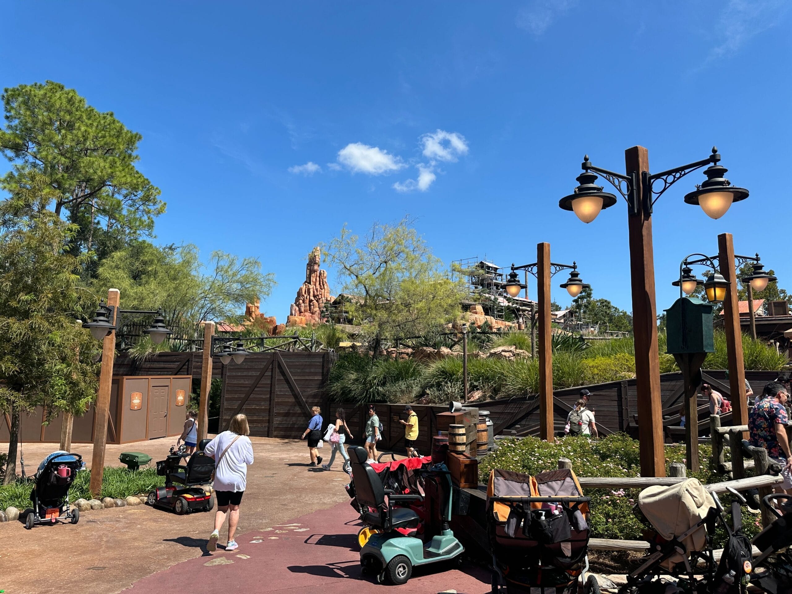 People walk near construction walls and strollers, with Disney World's Big Thunder Mountain under refurbishment in the background.