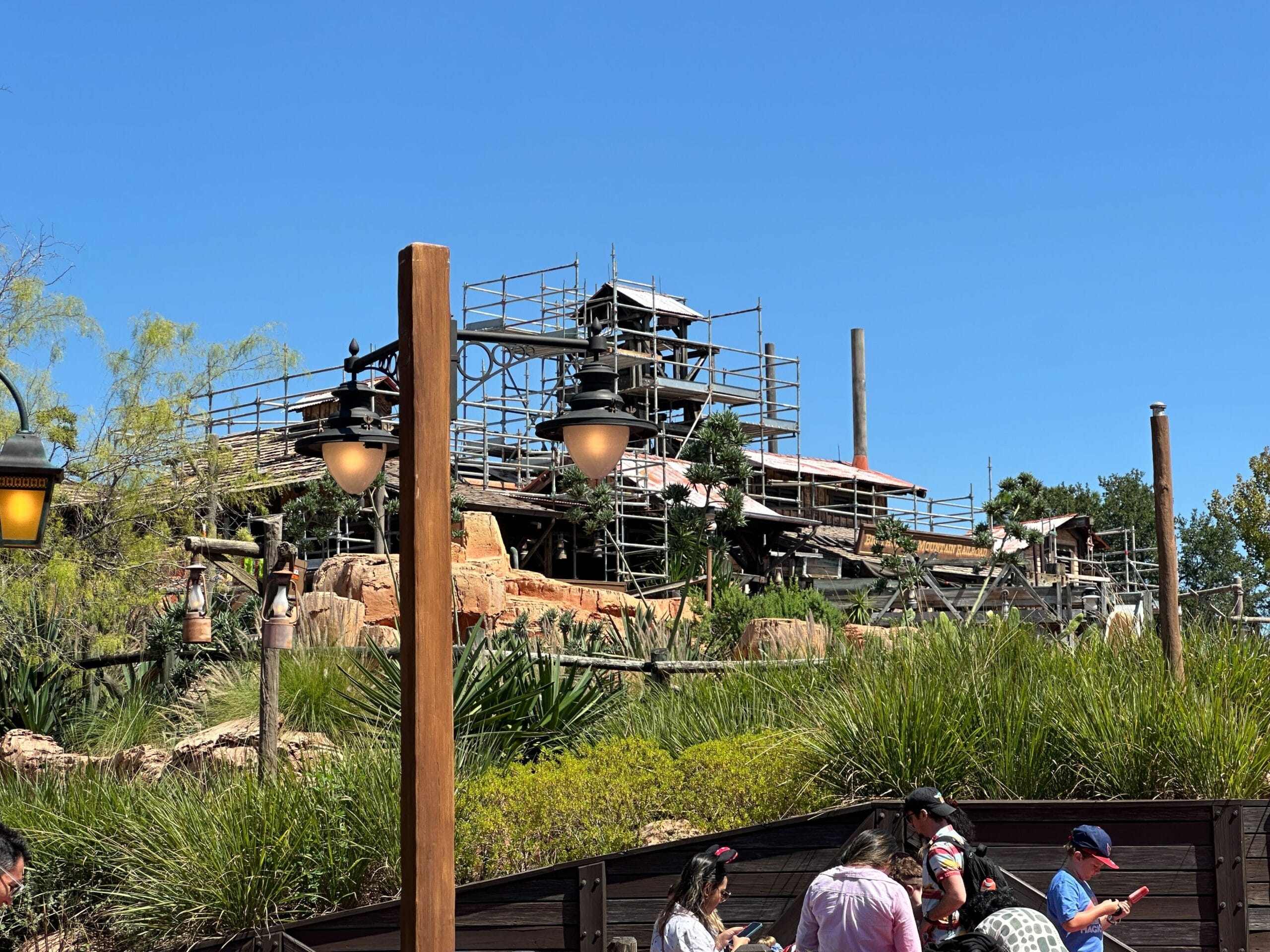 Big Thunder Mountain ride under refurbishment with scaffolding, greenery, and crowds beneath a clear blue Disney World sky.