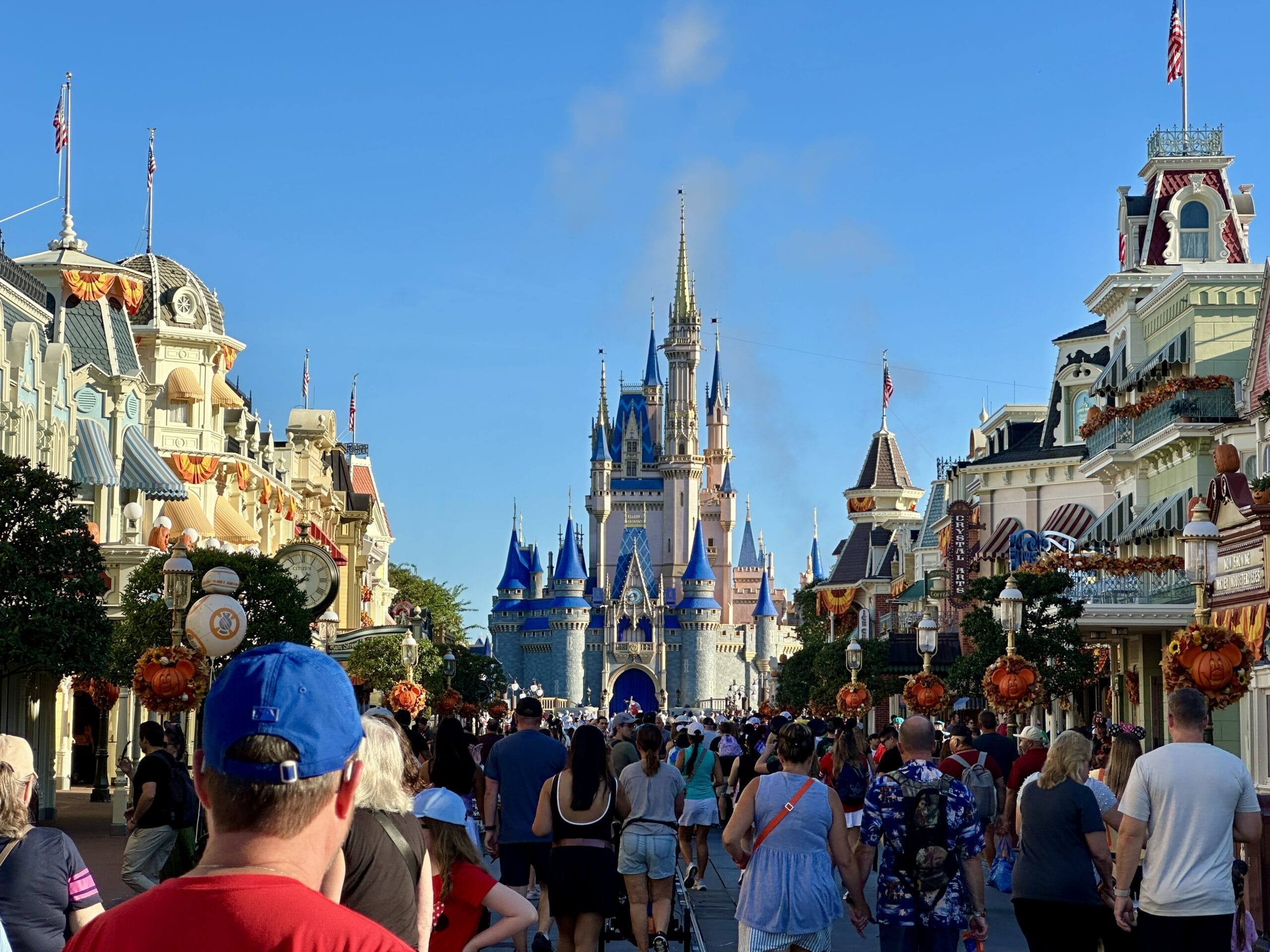 A crowd heads toward Cinderella Castle in Magic Kingdom at Disney World on a sunny day with blue skies.