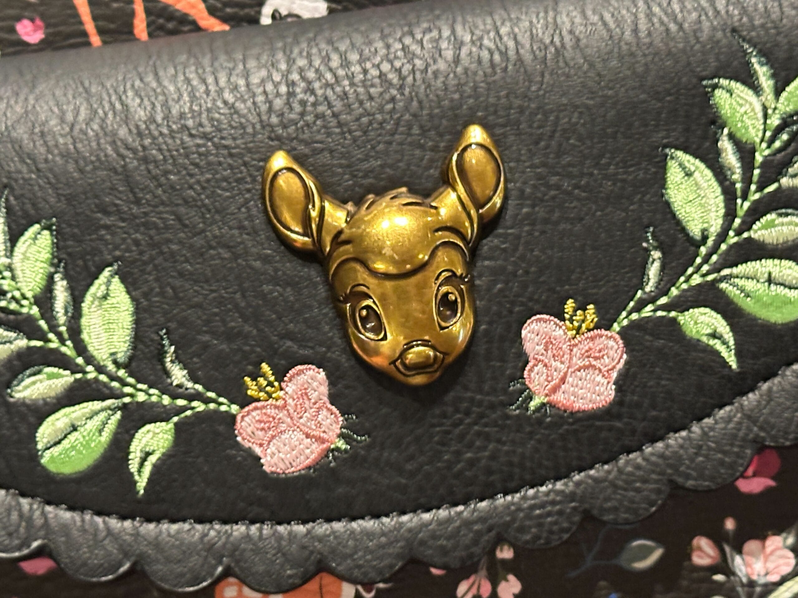 Close-up of a black Bambi Loungefly mini backpack with a gold face clasp and embroidered flowers and leaves.