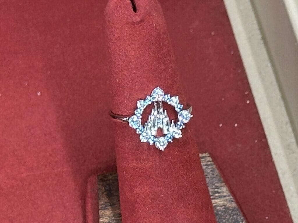 A Fine Jewelry diamond ring priced at $135 sits on red velvet inside a glass case, fit for Cinderella Castle.