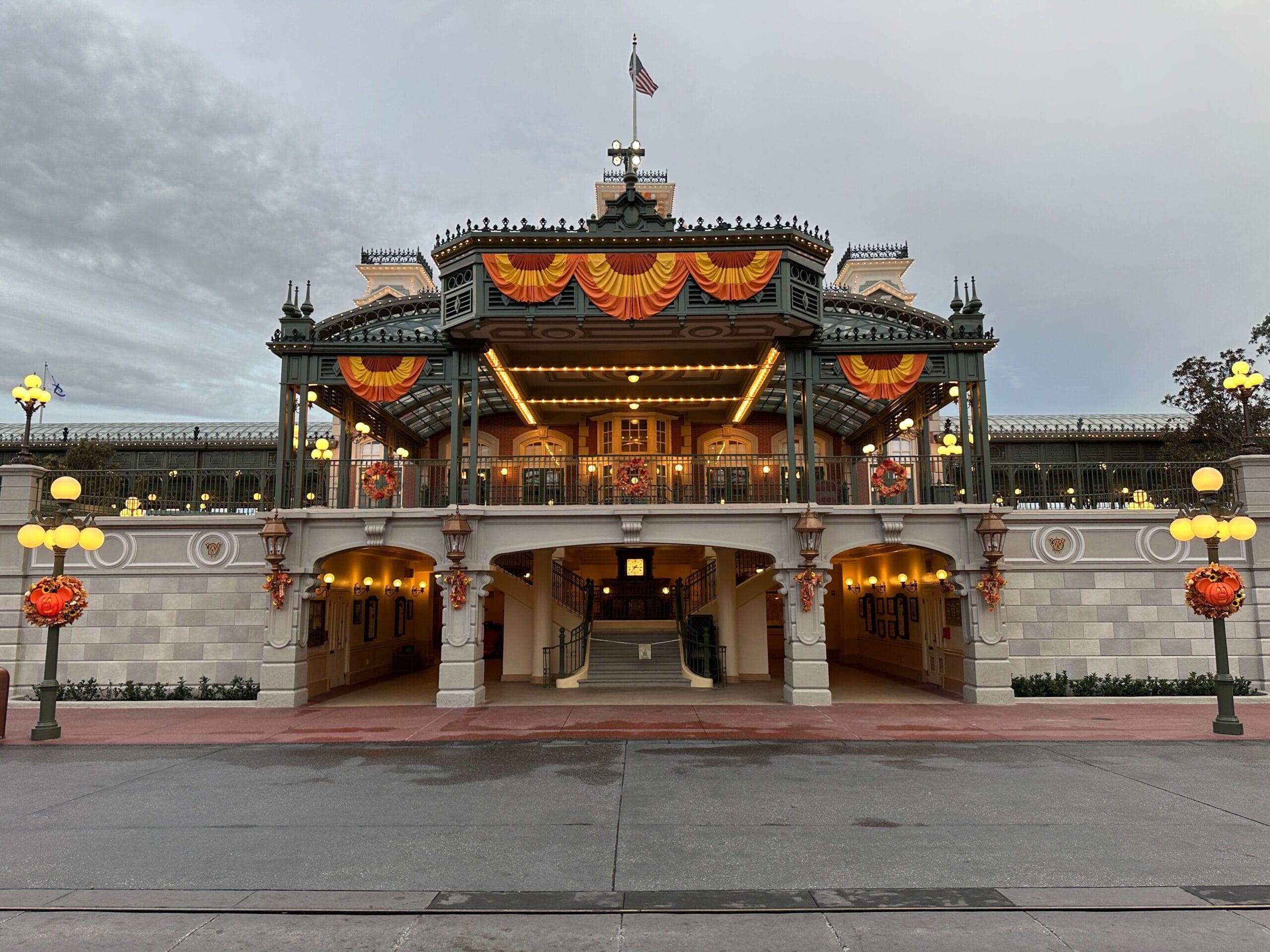 The entrance to a decorated theme park train station with orange and yellow autumn banners and lights.
