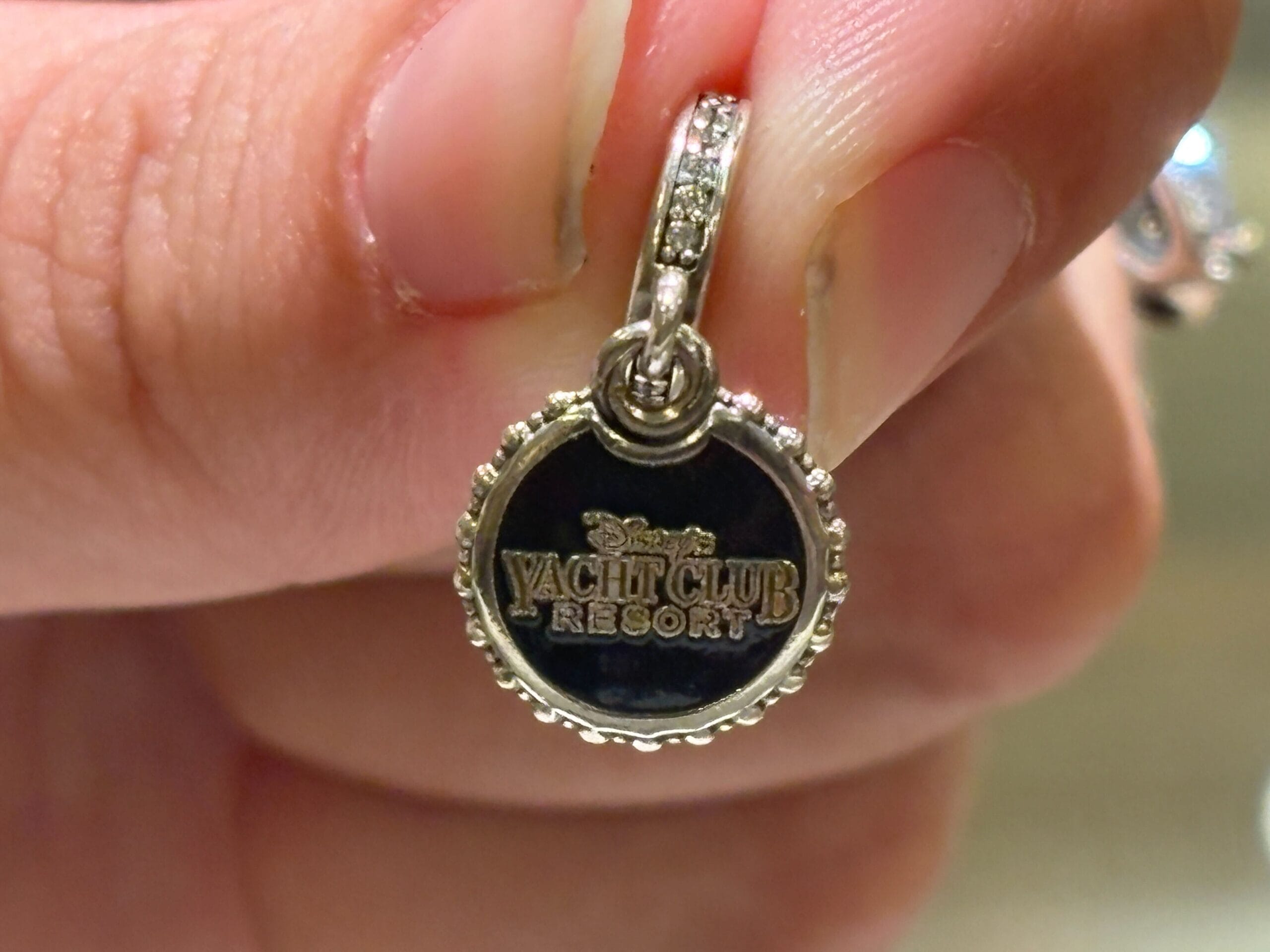 A hand holds a small Disney Yacht Club Resort charm with silver details and black enamel center.