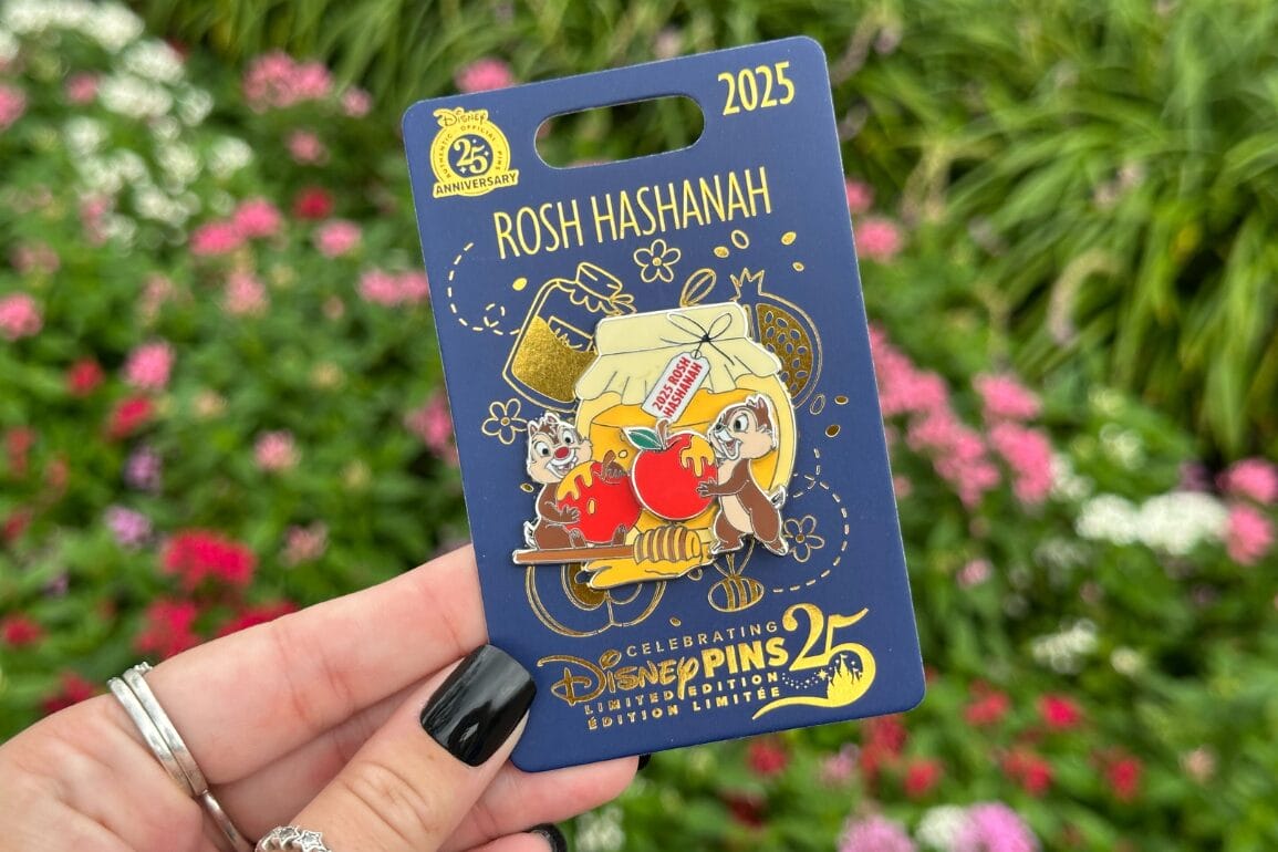 A hand holds a Disney Rosh Hashanah pin with Chip, Dale, honey, apples, and flowers—perfect for Stitch fans.