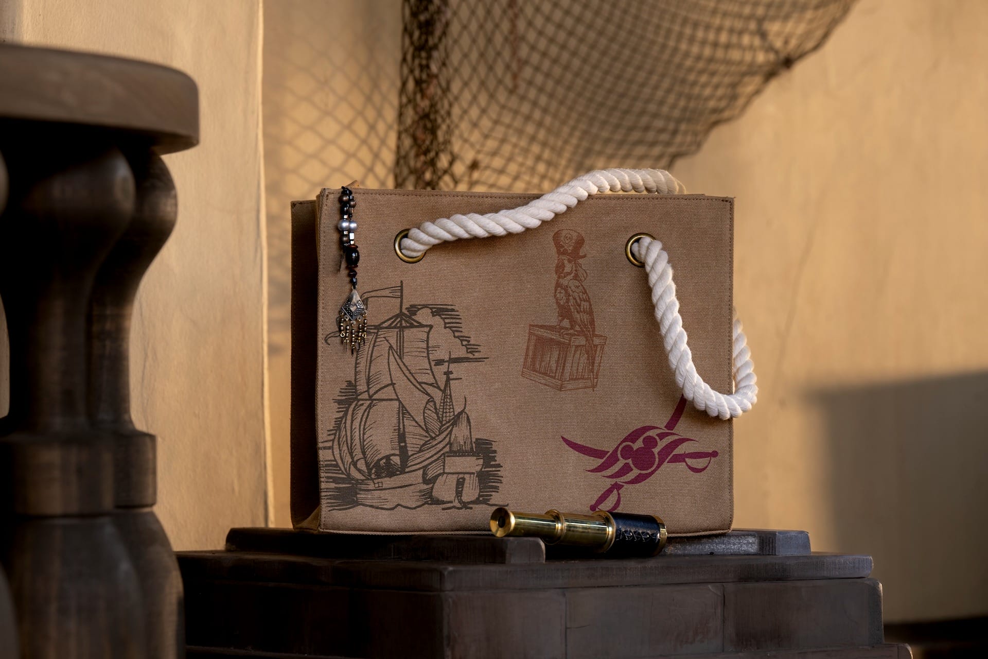 A decorative paper bag with rope handles, Disney Destiny nautical sketches, and pirates merchandise on a wooden surface.