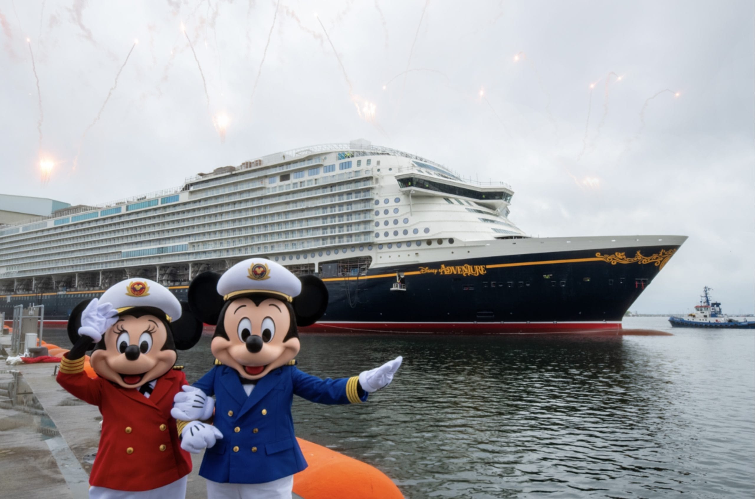 Mickey and Minnie Mouse in captain uniforms wave in front of a large cruise ship with fireworks in the sky.