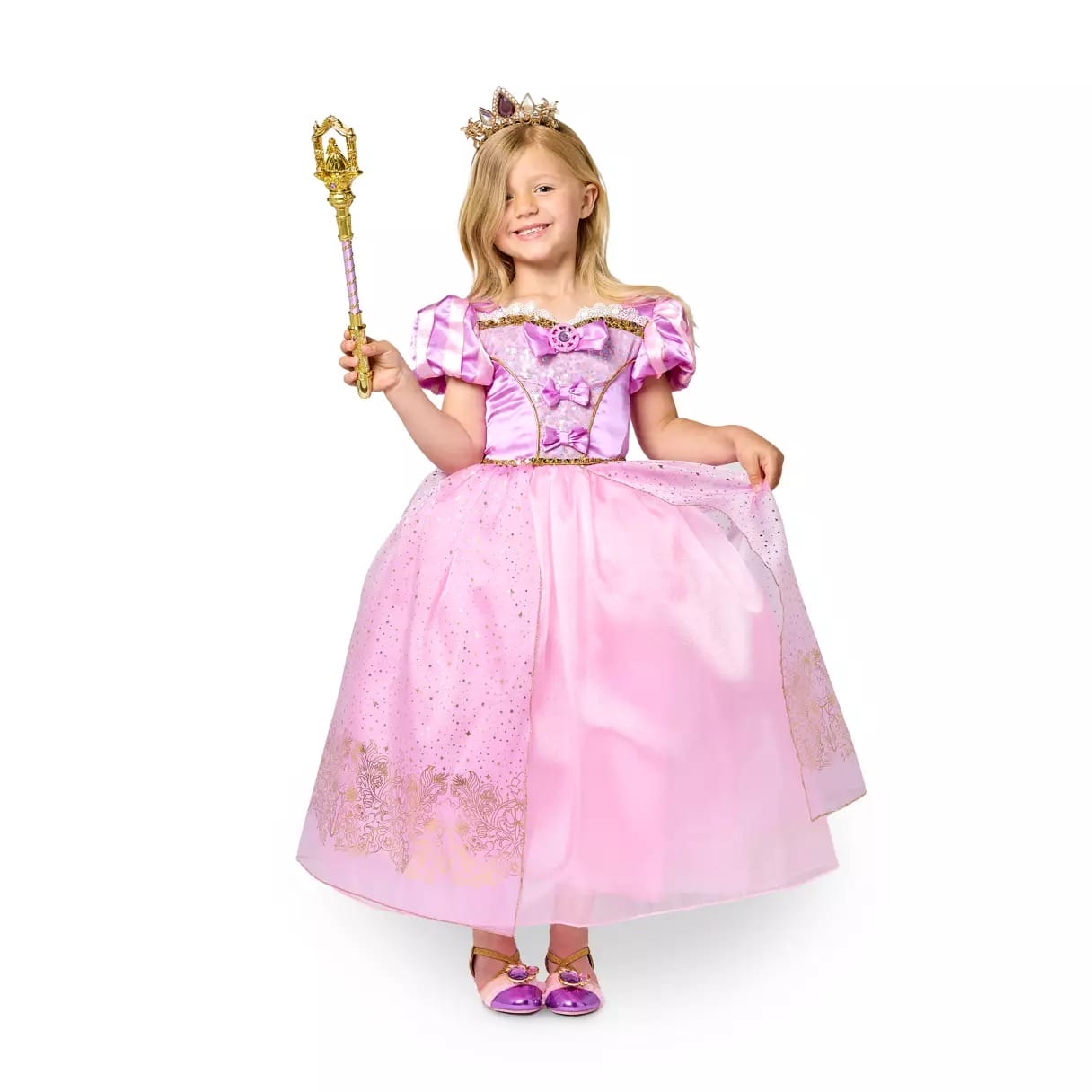 Smiling girl in a pink princess dress from Disney Store, holding a jeweled wand and wearing a tiara, stands against white.