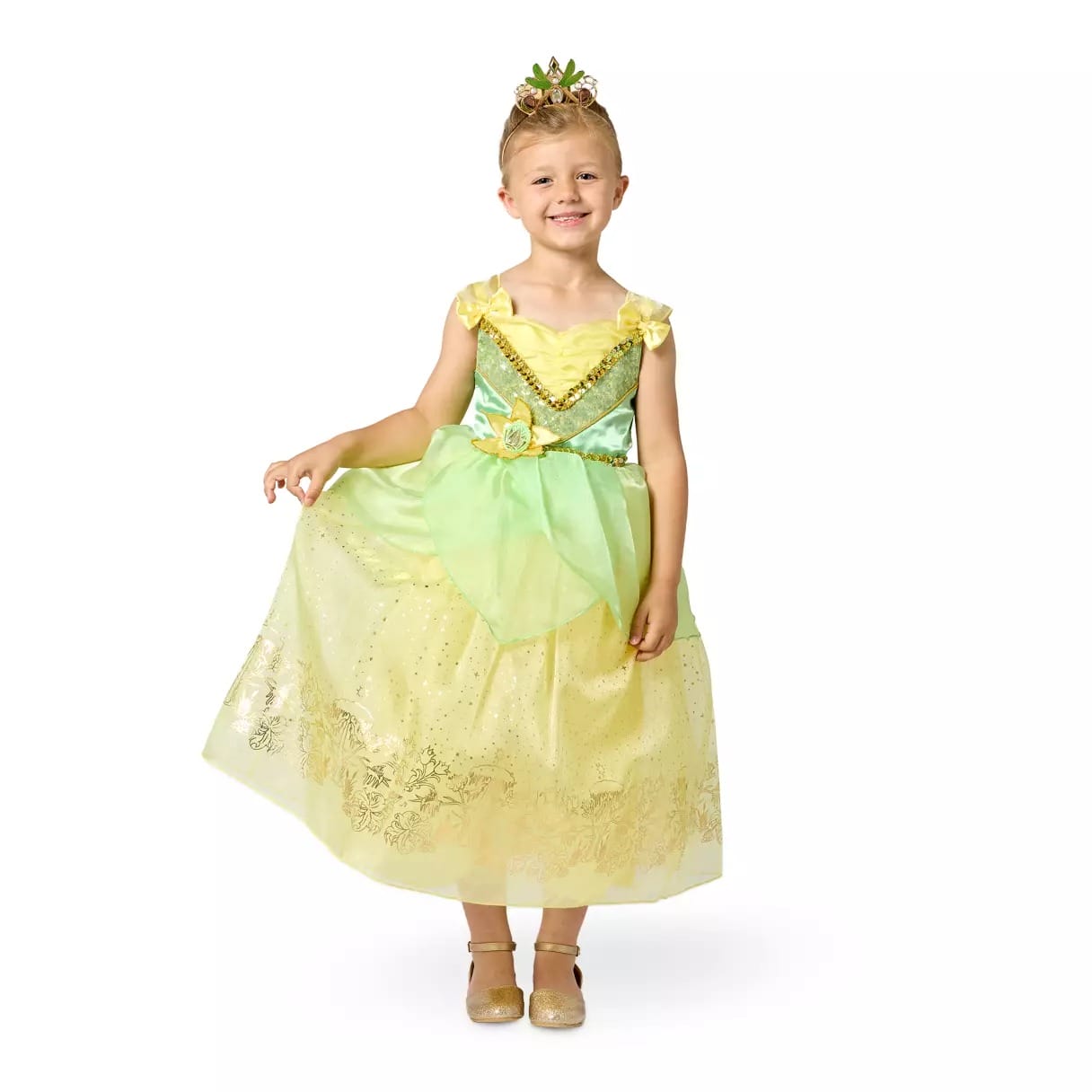 Smiling child in a Disney Store princess dress and tiara, holding out the skirt, standing against a white background.