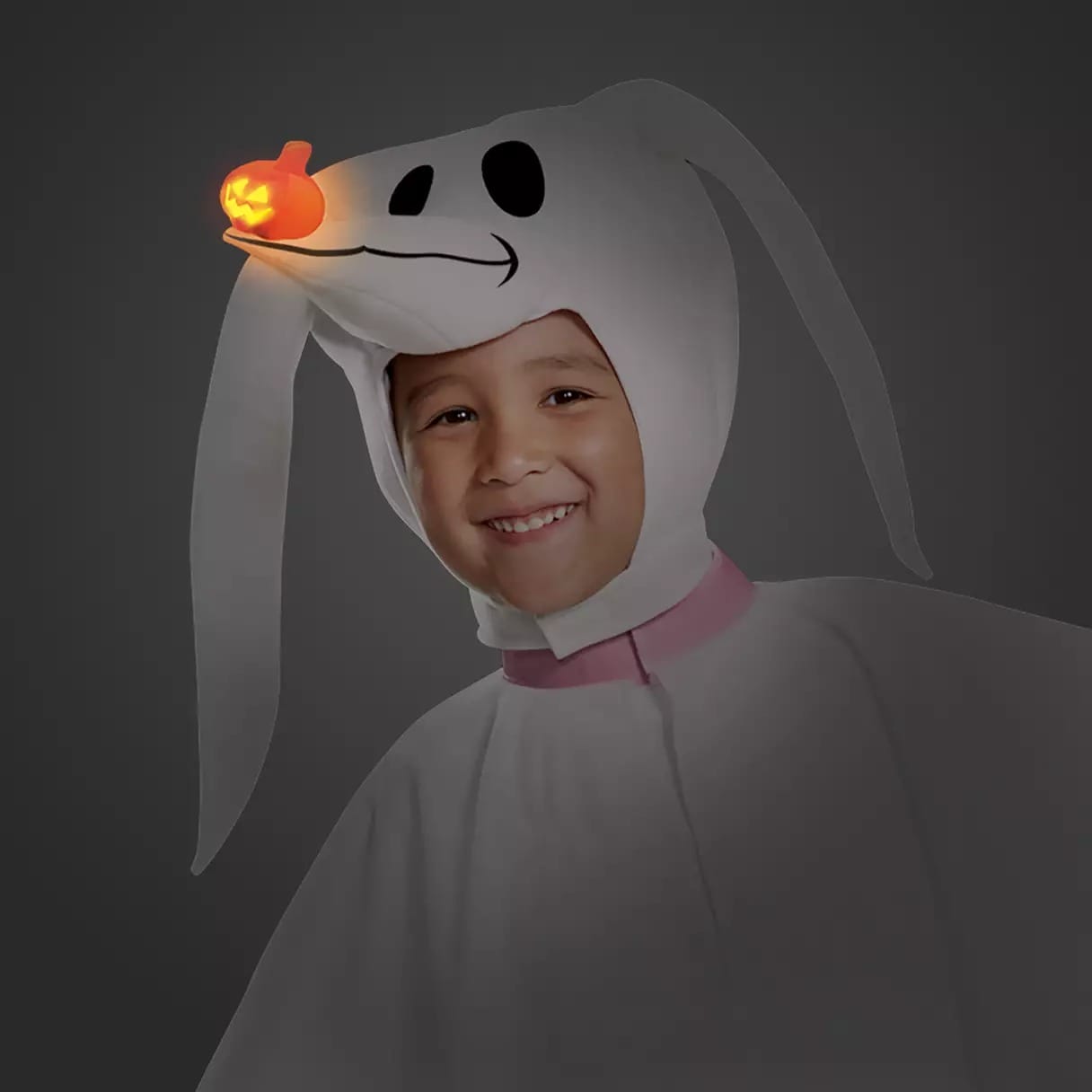 Smiling child in a Disney Store Zero the ghost dog Halloween costume with a glowing pumpkin nose headpiece.