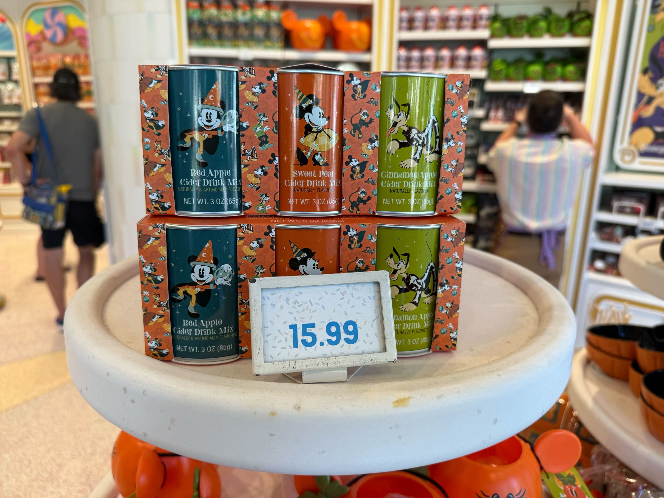 Six Disney-themed drink mix tins on display at Disneyland; Halloween merchandise features Mickey, Minnie, Goofy, and Pluto at $15.99.