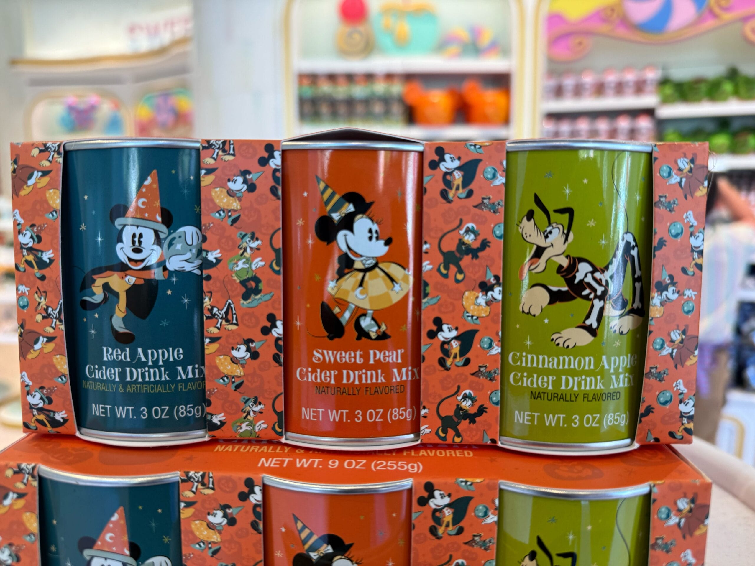 Three colorful Disney-themed cans of apple cider drink mix—perfect Halloween merchandise for any Disneyland fan.