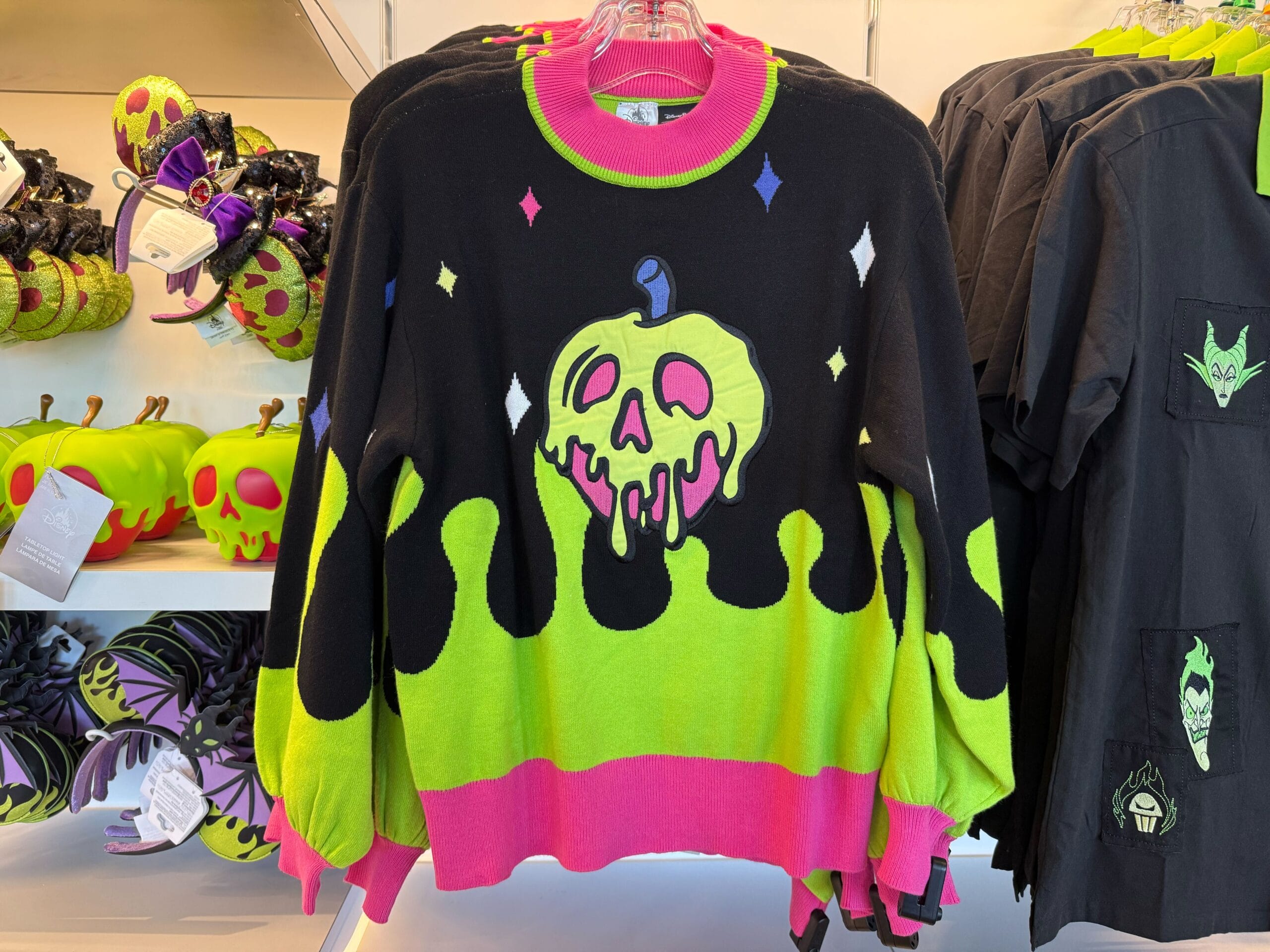 Black sweater with neon dripping poison apple design, part of Disneyland Villains merchandise on a themed store rack.