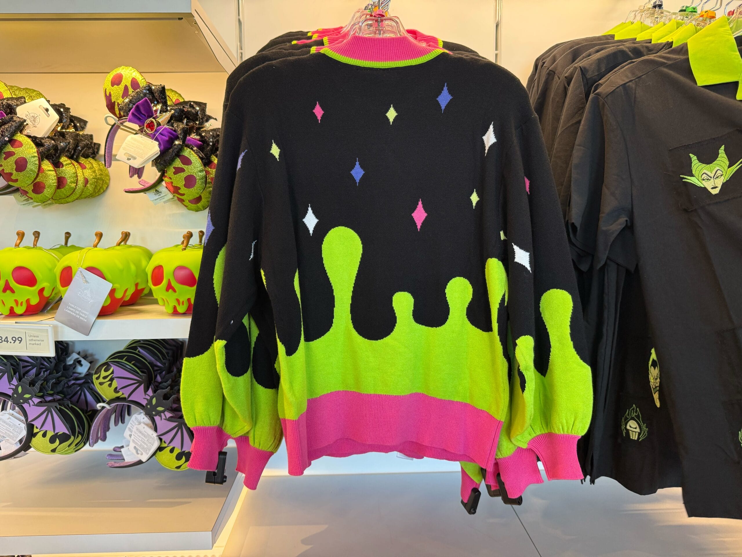 A black sweater with neon drips and diamonds hangs in a store, perfect as eye-catching Villains merchandise.
