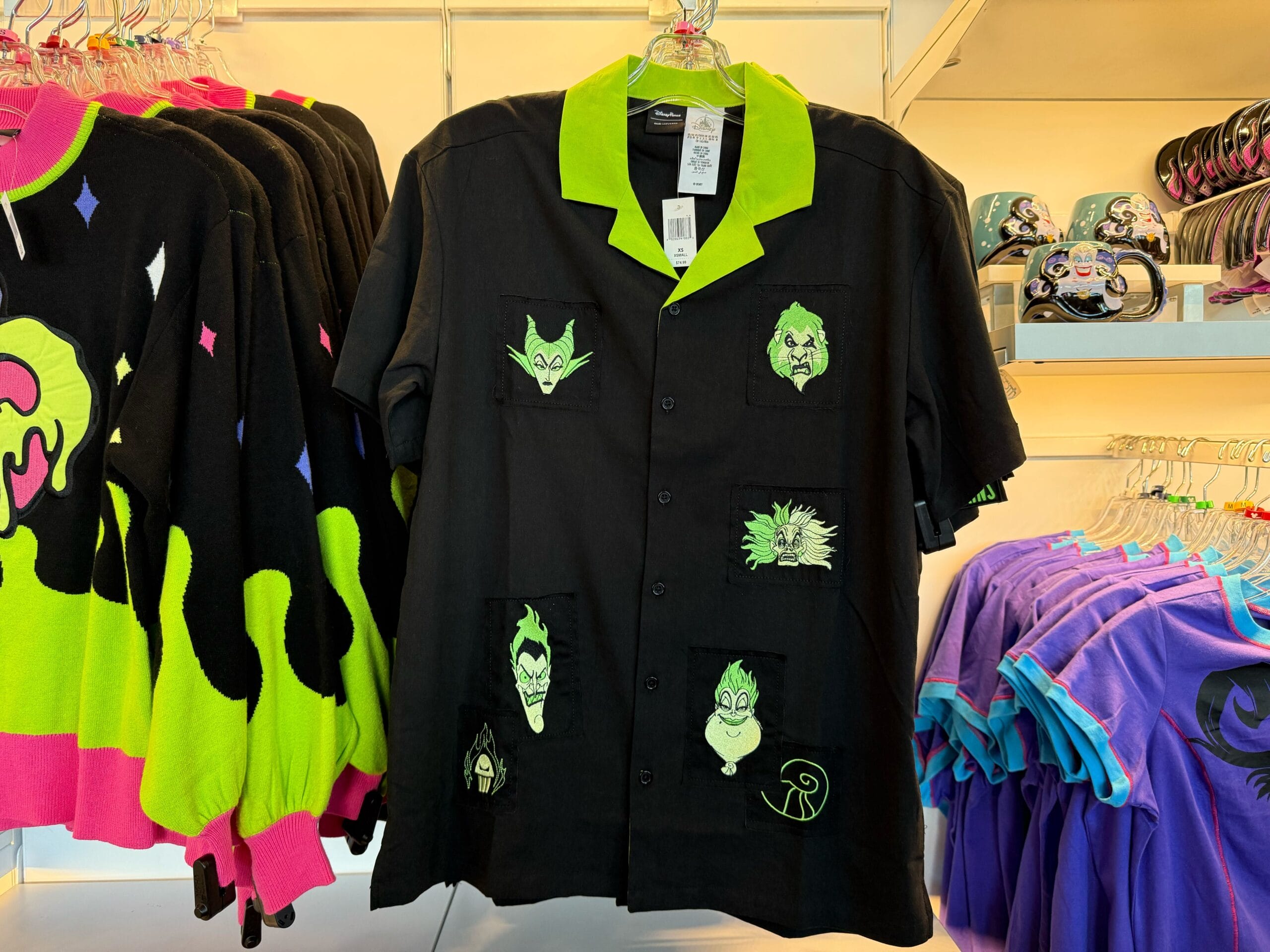 Black button-up shirt with green collar featuring embroidered Disney villains, perfect Halloween merchandise on display rack.